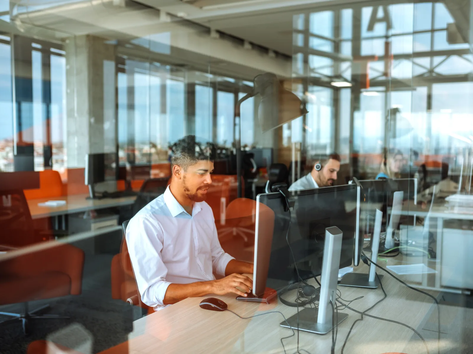Man working on desktop computer in modern office with glass walls and reflected city view outside