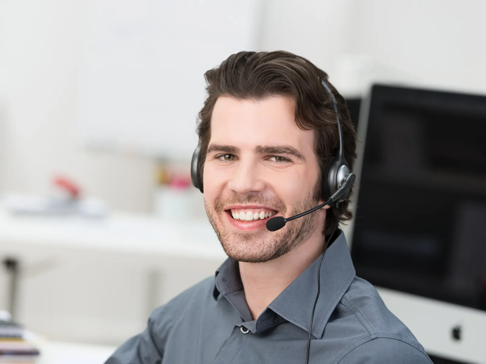 Smiling male customer service representative wearing headset in modern office environment