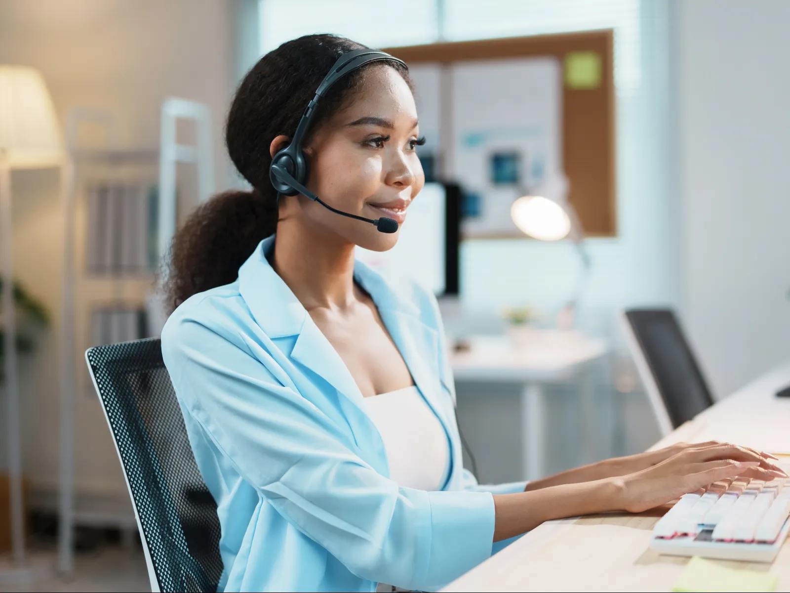 Customer support agent wearing headset typing on keyboard in modern office environment