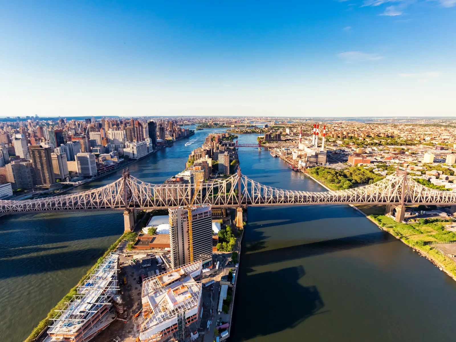 Aerial view of Queensboro Bridge over East River with Manhattan skyline and sunny blue sky in New York City
