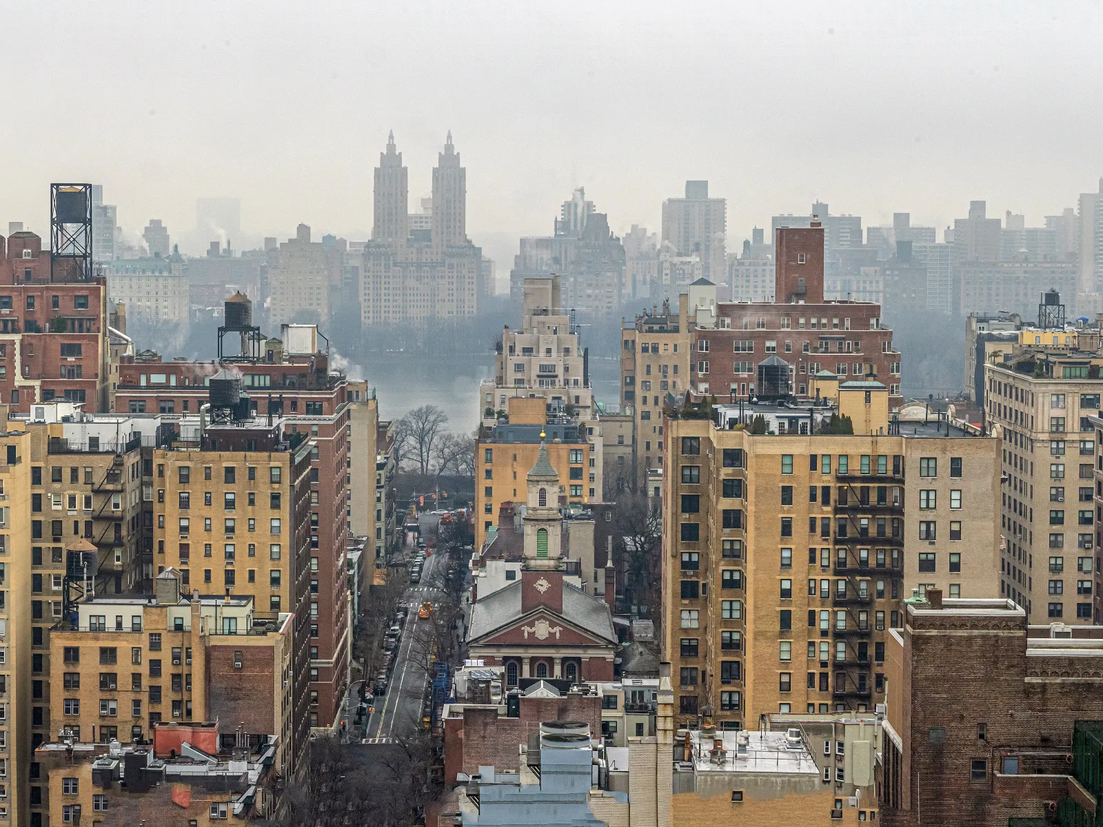 Foggy cityscape with densely packed mid-rise buildings and distant skyscrapers under overcast sky