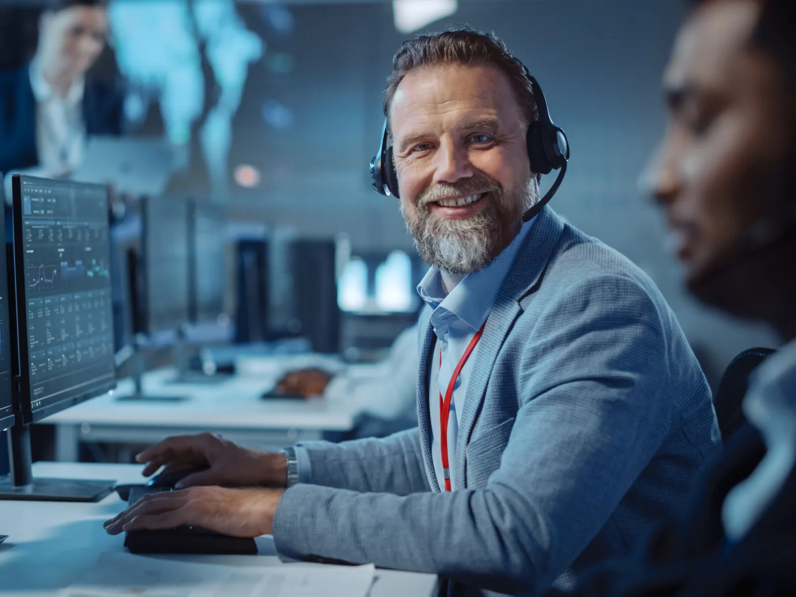 Smiling customer support agent with headset working on dual monitors displaying data analytics in modern office.