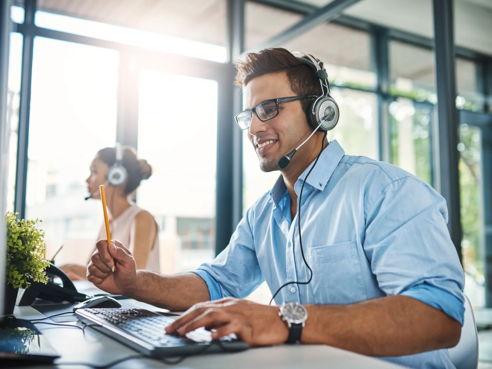 Smiling customer service representatives wearing headsets working in a modern, bright office environment.