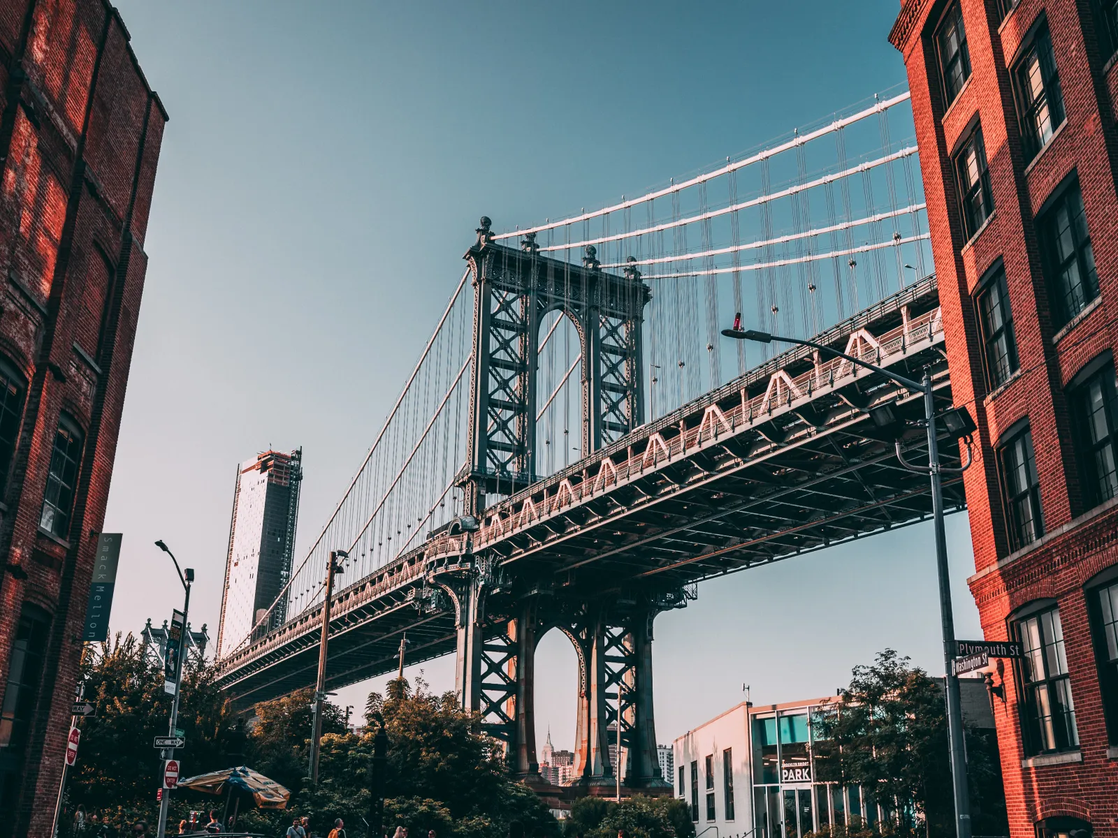 View of the Manhattan Bridge framed by red brick buildings against a clear blue sky in New York City.