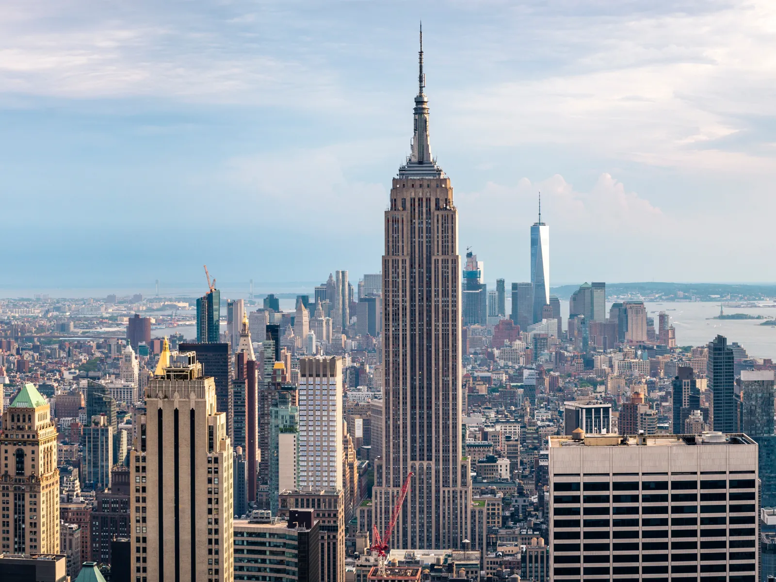 Panoramic view of New York City skyline featuring Empire State Building and surrounding skyscrapers under cloudy sky.
