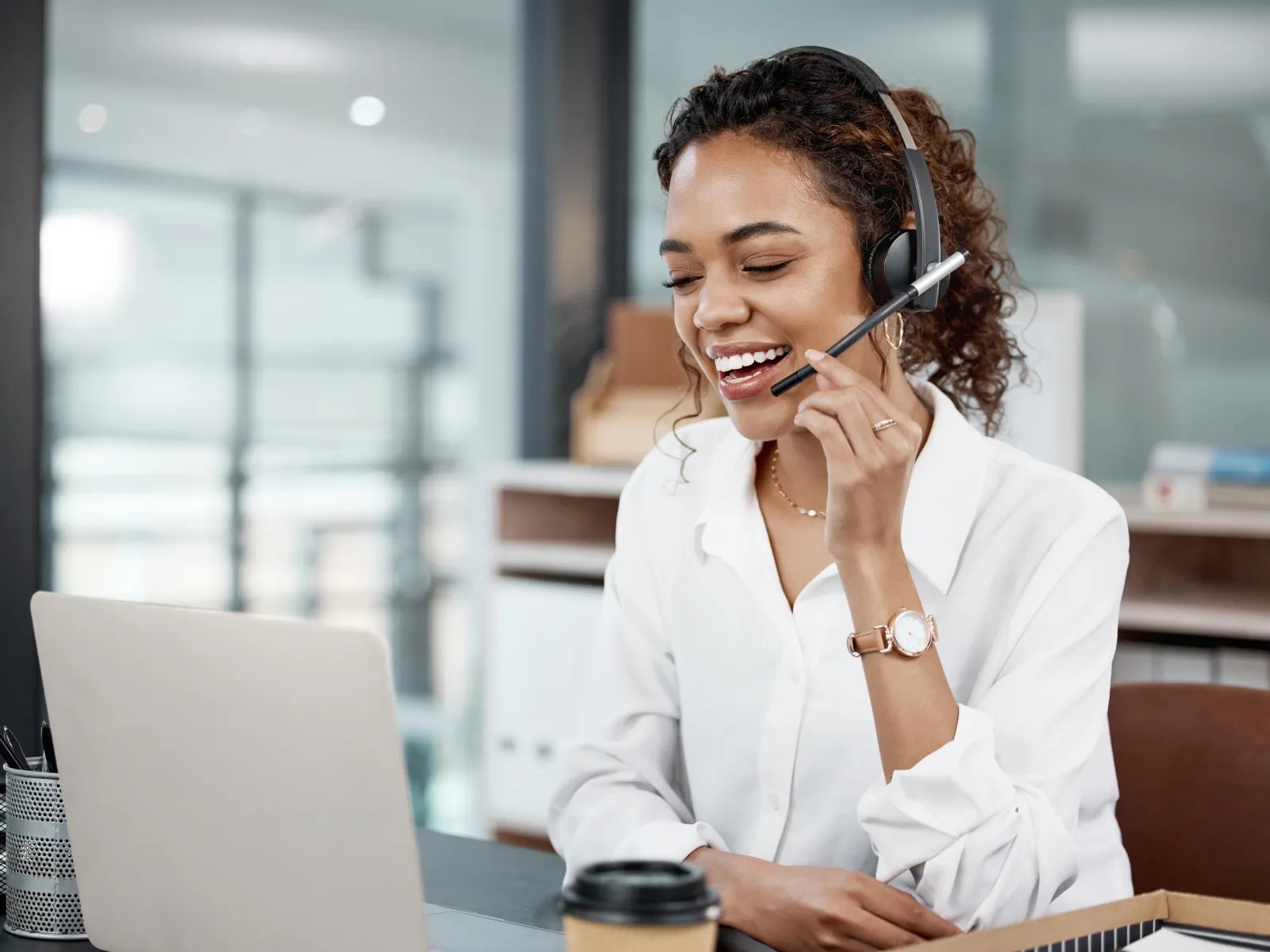 Smiling customer service representative wearing headset talks on laptop in modern office setting