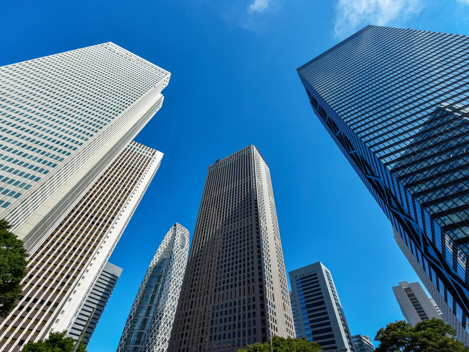 Low-angle view of modern skyscrapers with glass and concrete facades under a clear blue sky.