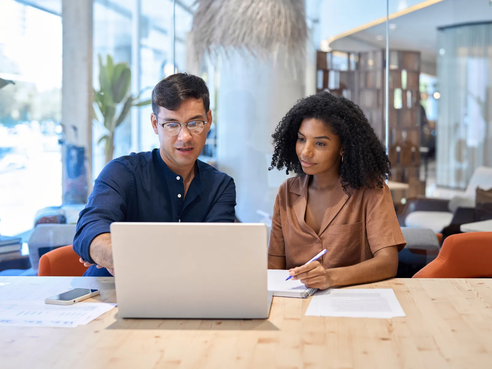Man and woman collaborating on laptop in modern office with documents and notes on wooden table