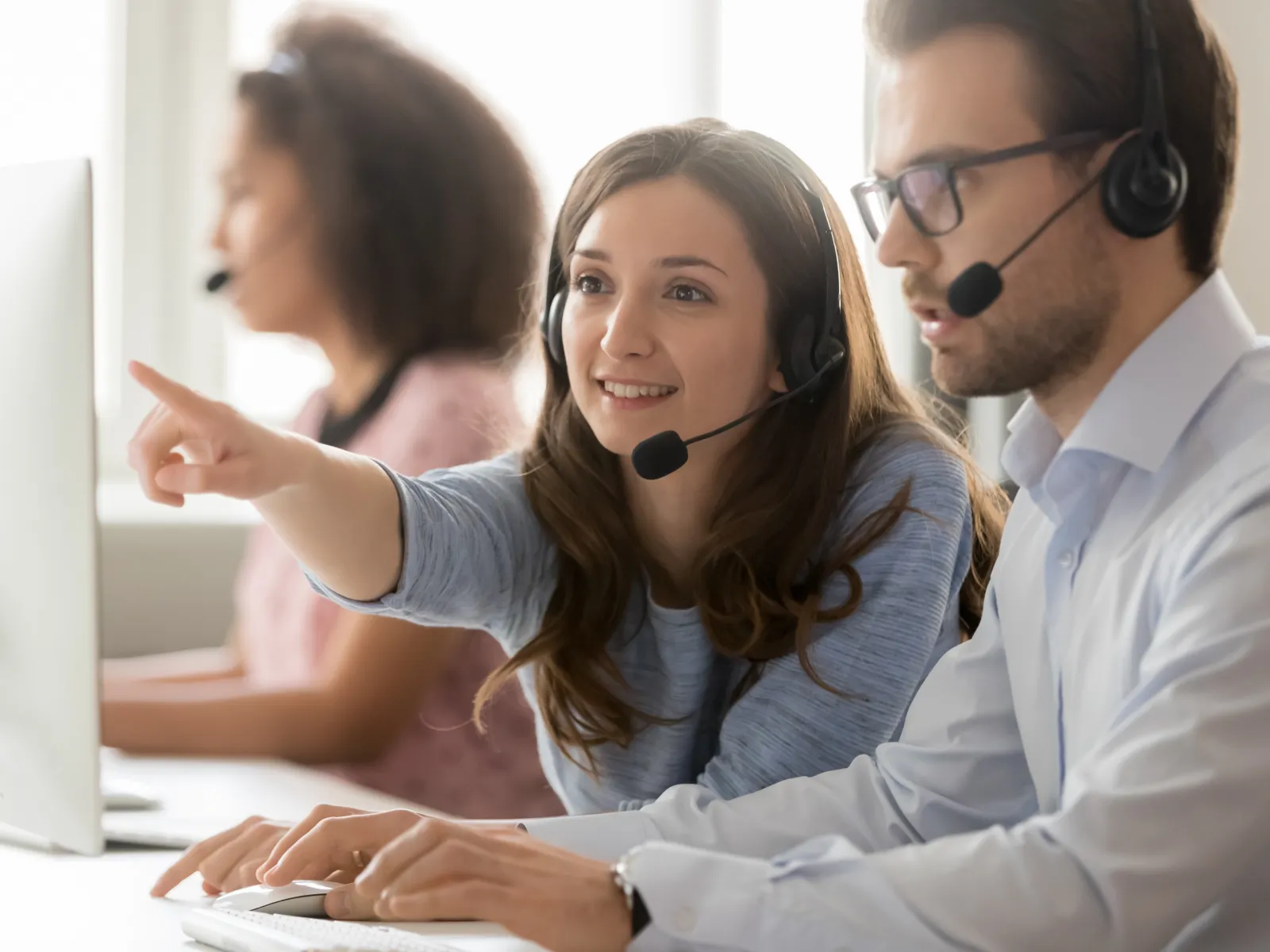 Customer support team members wearing headsets working together at computers in a bright office environment