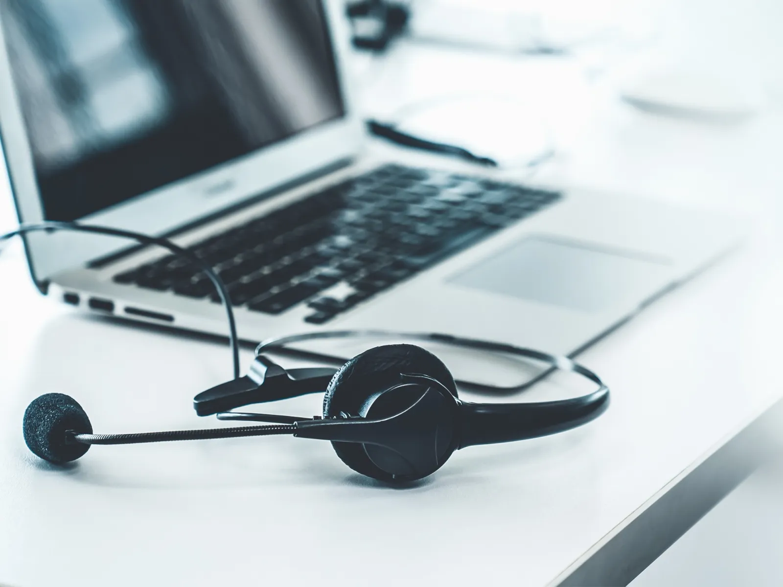 Black headset with microphone on white desk beside open laptop, symbolizing remote work or customer support.