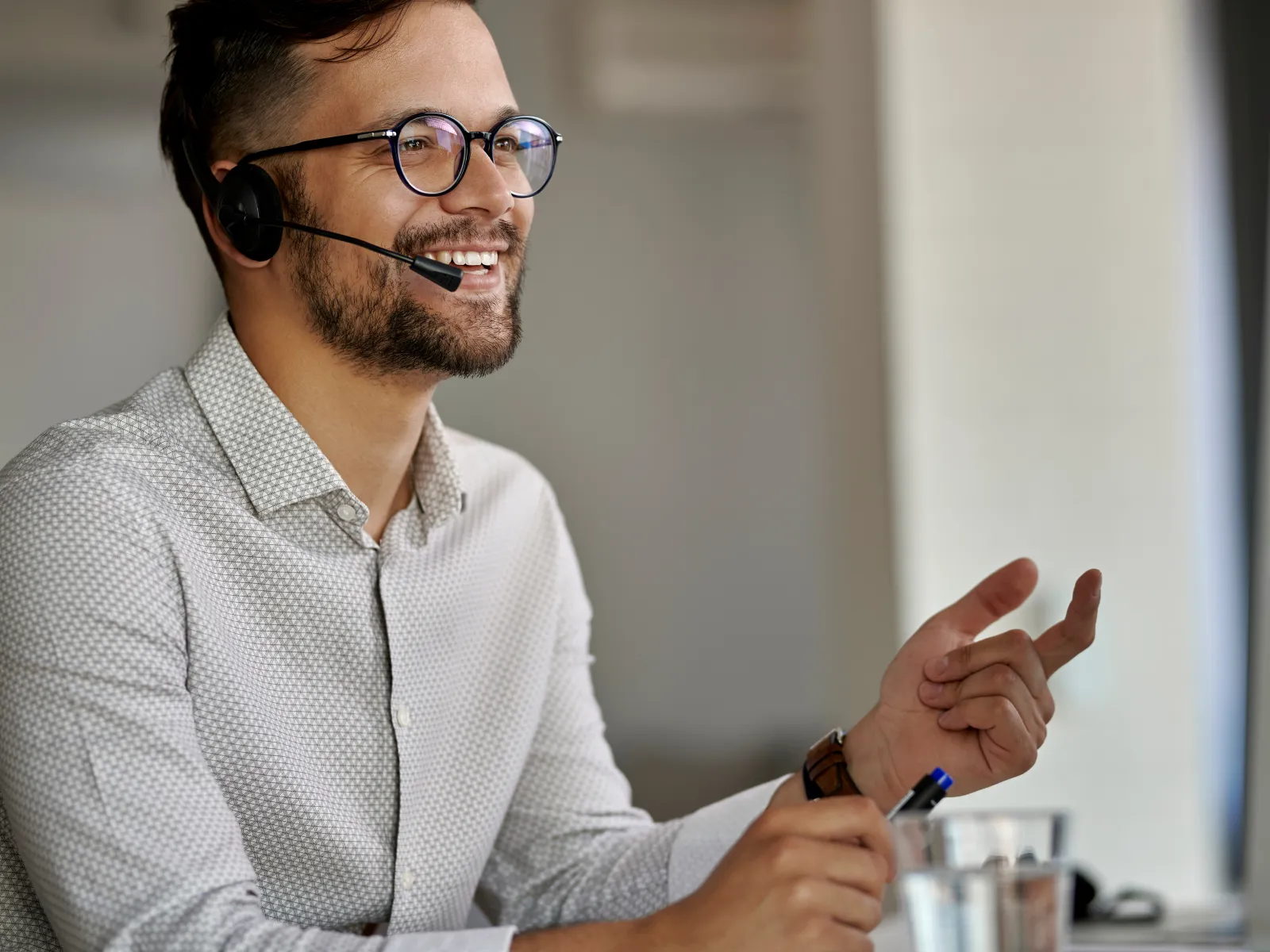 Young male customer service representative smiling wearing headset and glasses at office desk