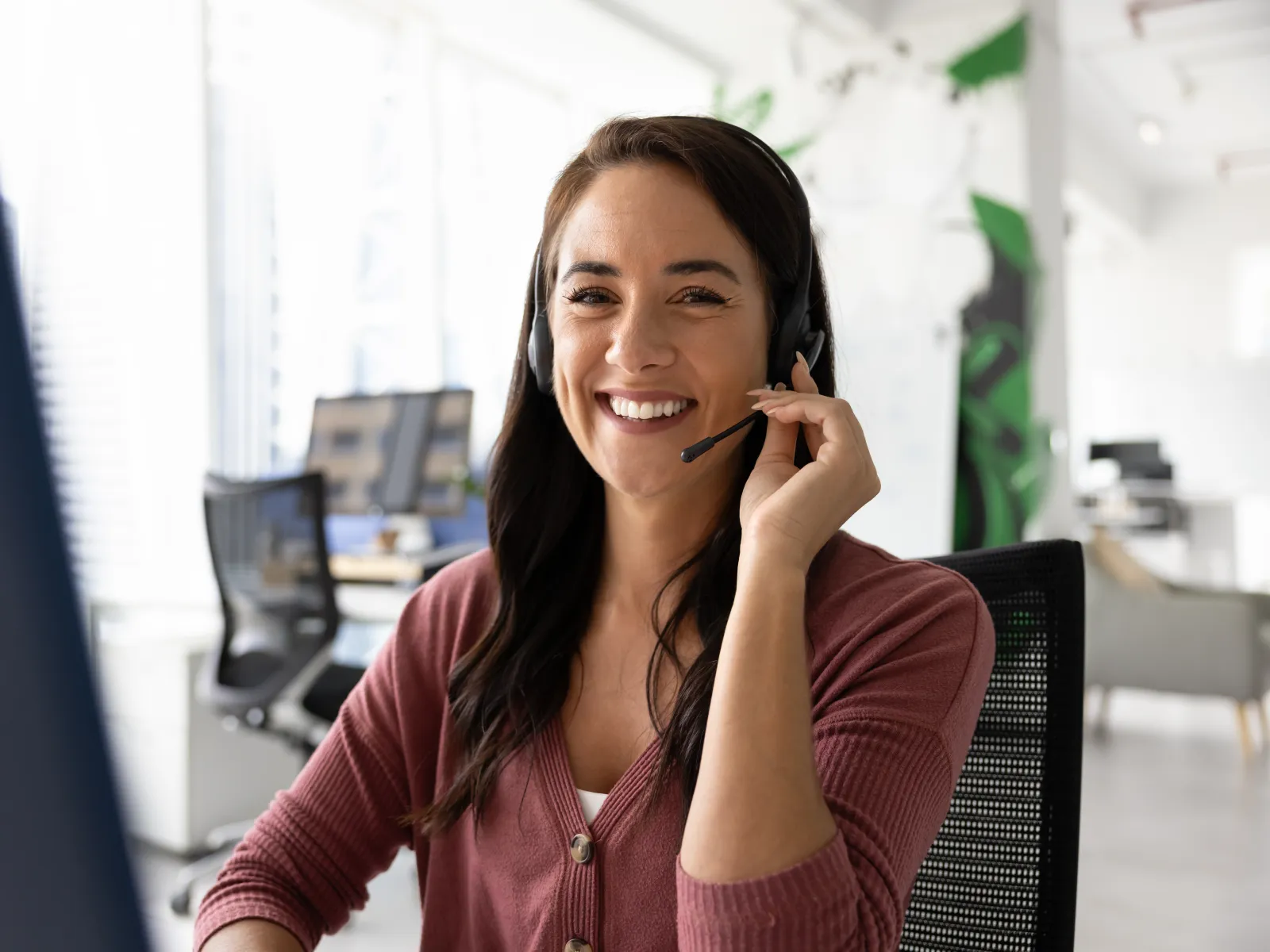 Smiling female customer service representative wearing headset working in modern office environment