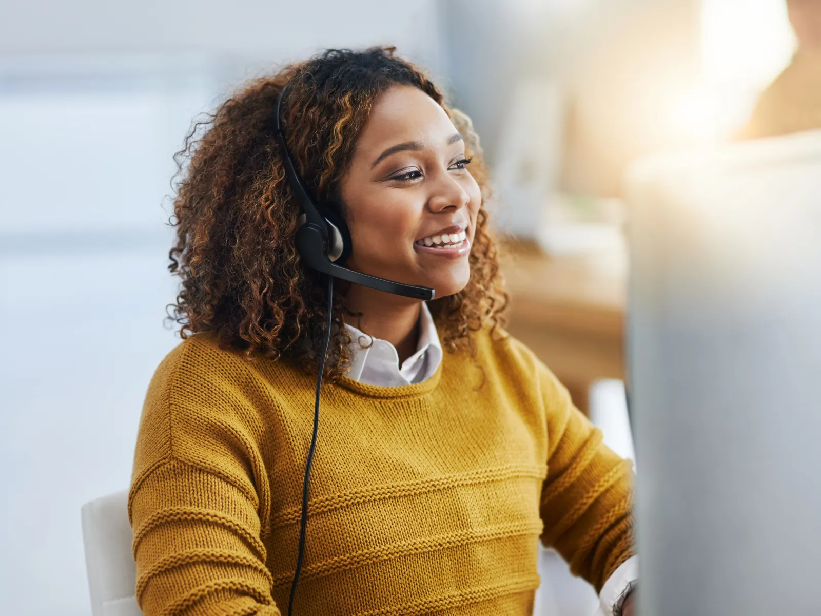 Smiling customer service representative wearing headset working on computer in bright office environment