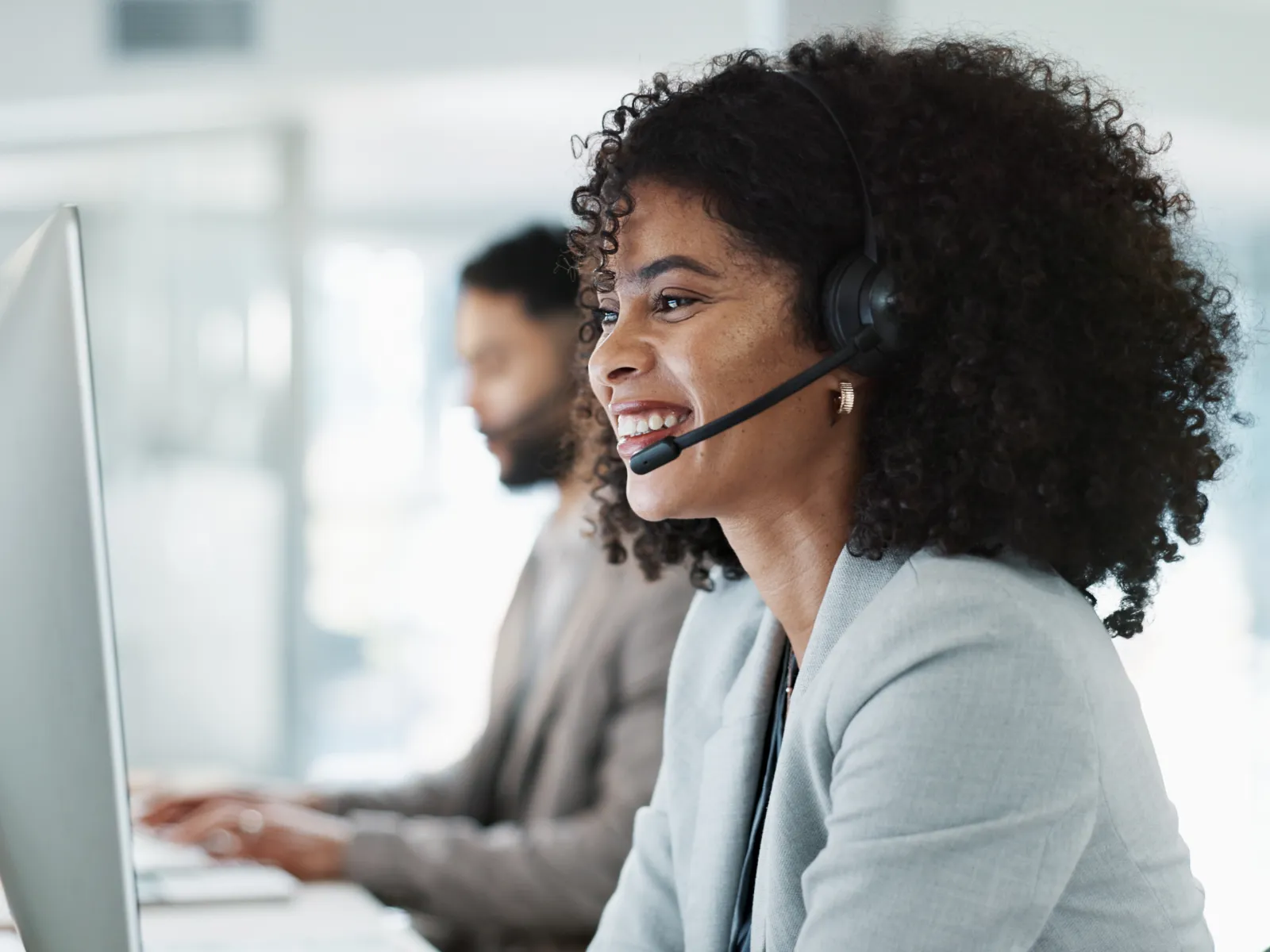 Smiling customer service representative wearing headset working at computer in modern office environment