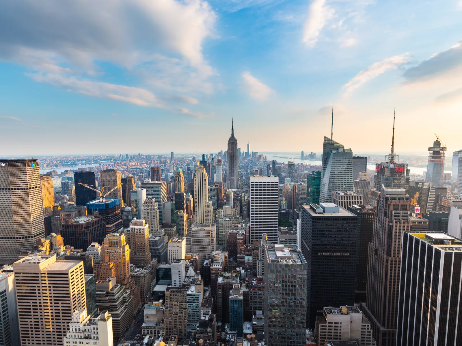 Aerial view of New York City skyline with iconic skyscrapers under a partly cloudy blue sky at sunset.