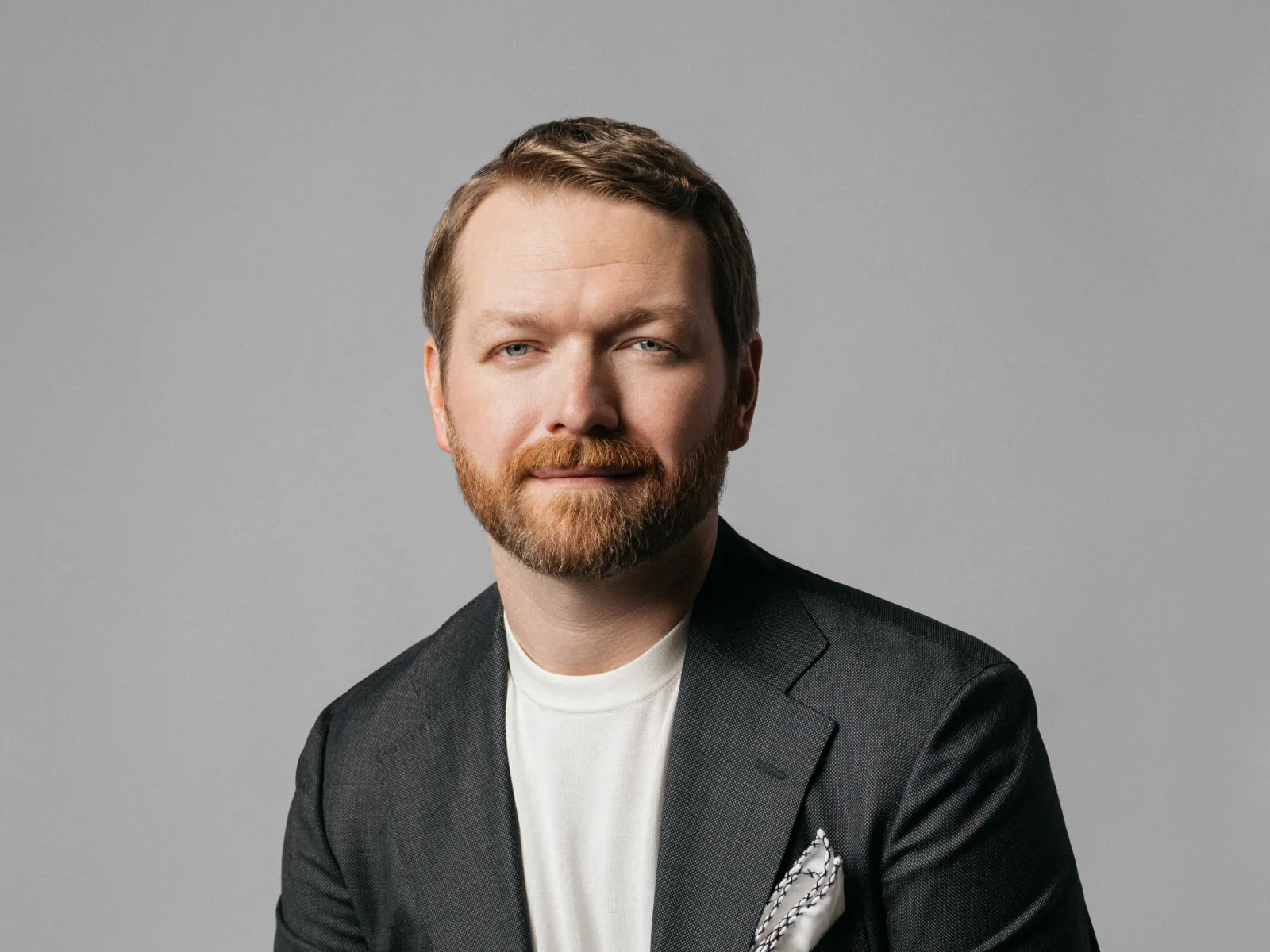 A man in a suit sits confidently, showcasing a professional demeanor against a neutral background.