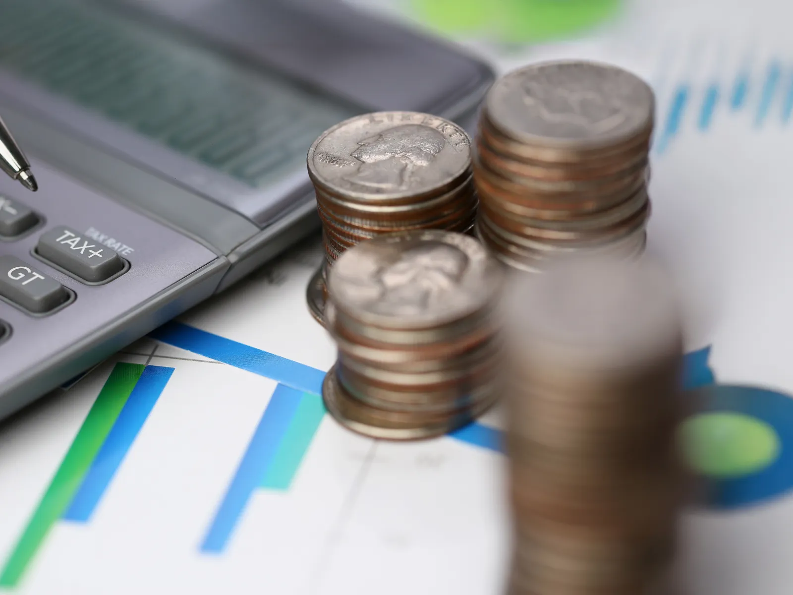 Stacks of coins next to a calculator and pen on financial charts depicting investment and budgeting concepts