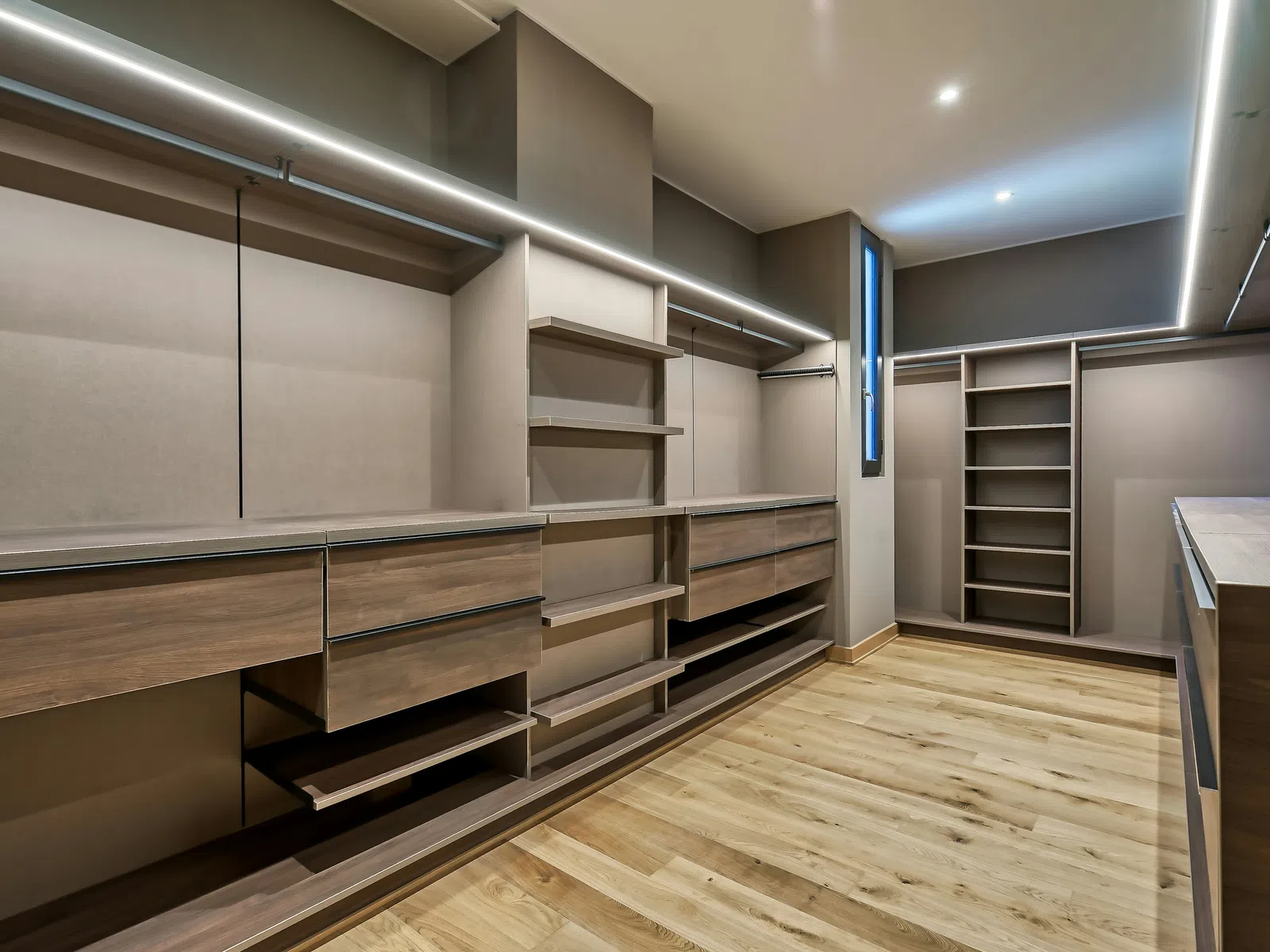 Modern spacious walk-in closet with wooden drawers, shelves, hanging rods, and recessed lighting.