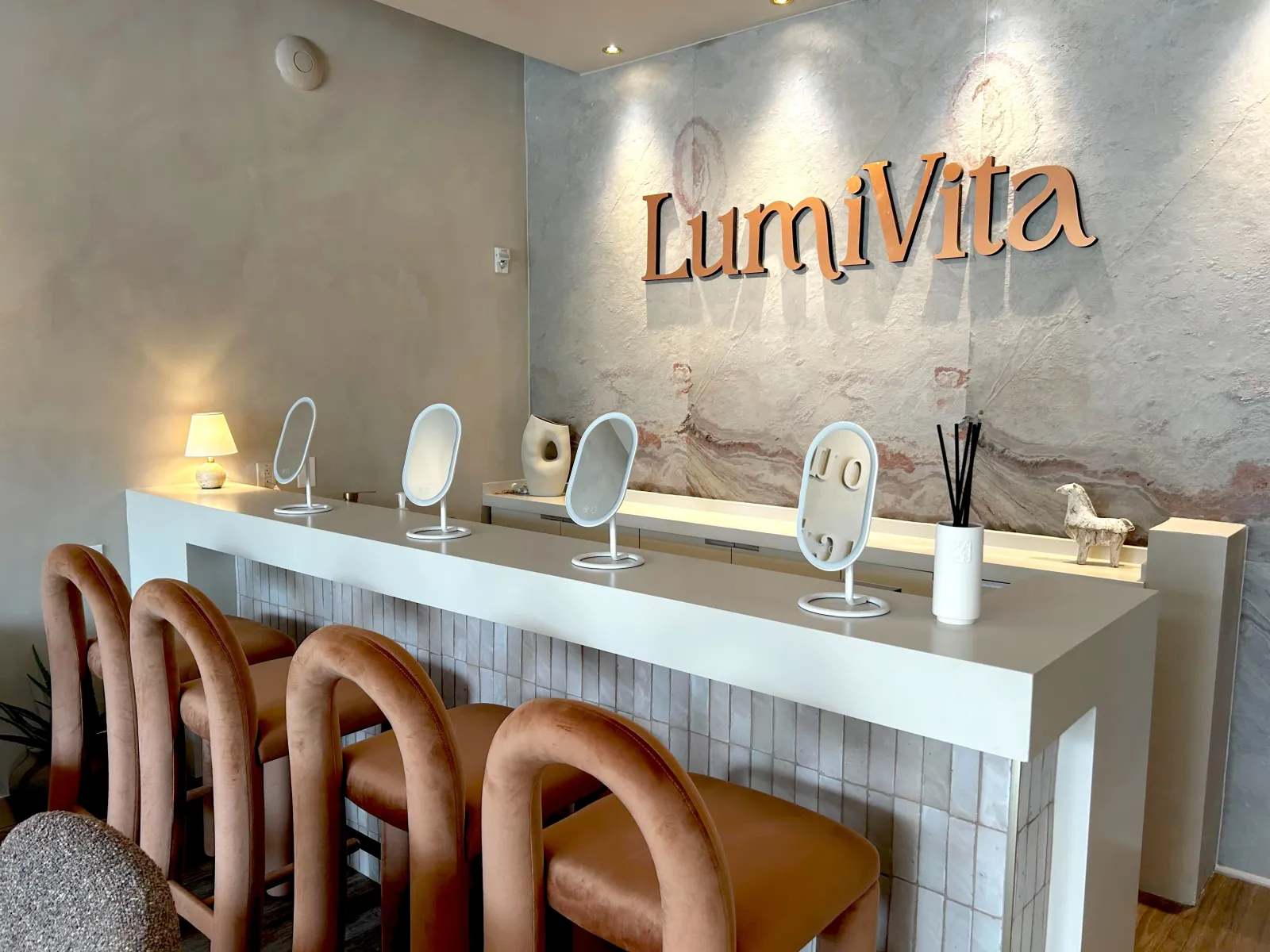 Modern salon interior with brown chairs, white countertop, mirrors, and LumiVita logo on textured wall.