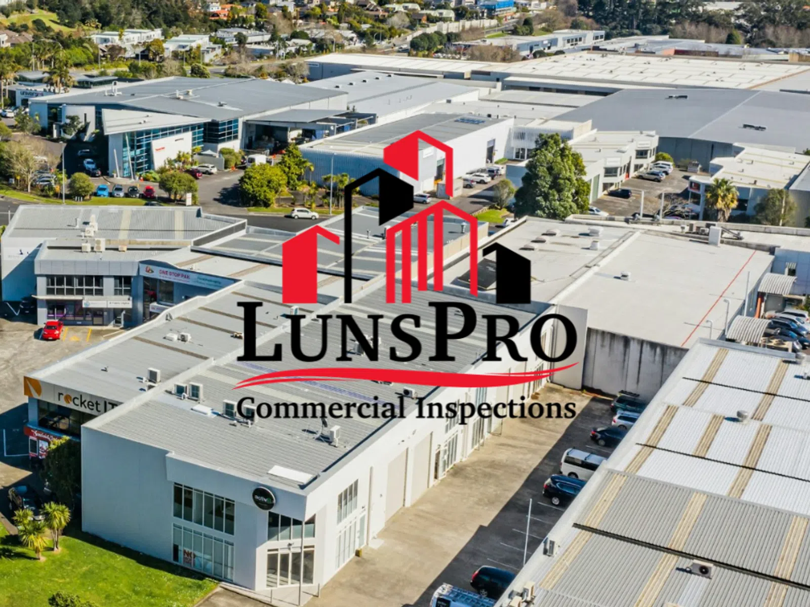 Aerial view of industrial commercial buildings under clear skies with LunsPro Commercial Inspections logo overlay.
