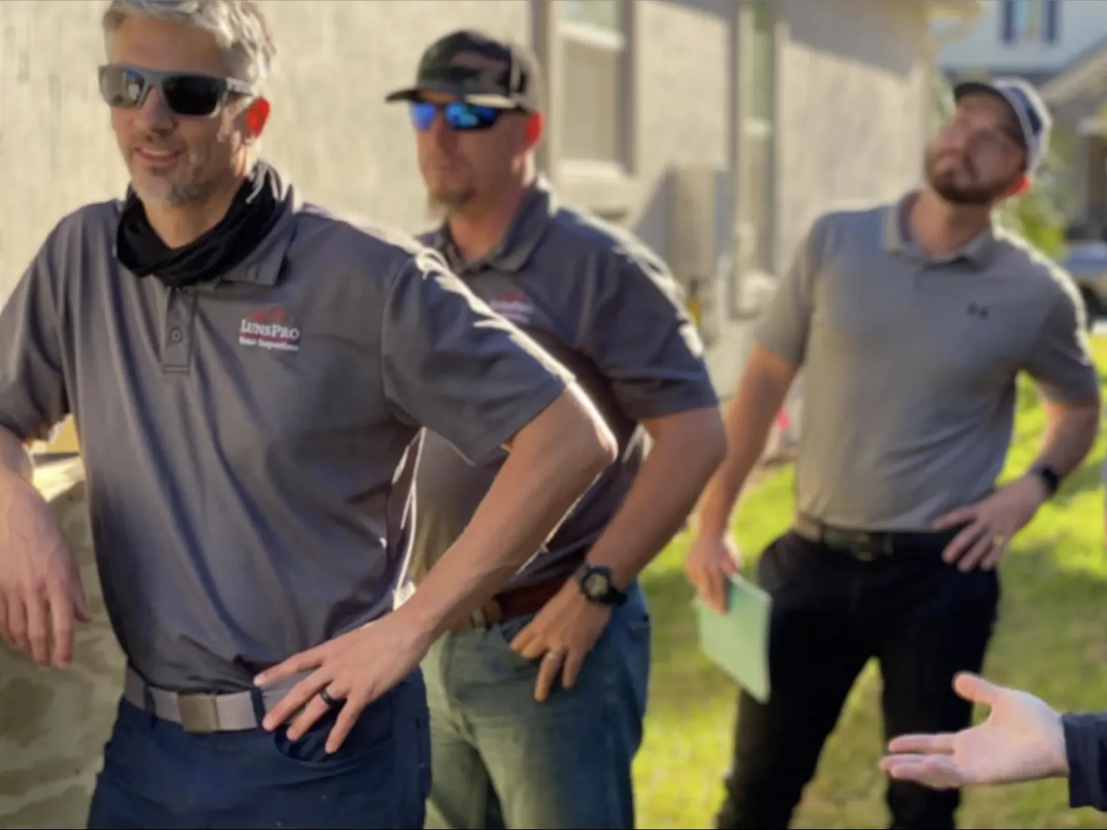 Group of men outdoors in casual work attire discussing near a building in bright daylight