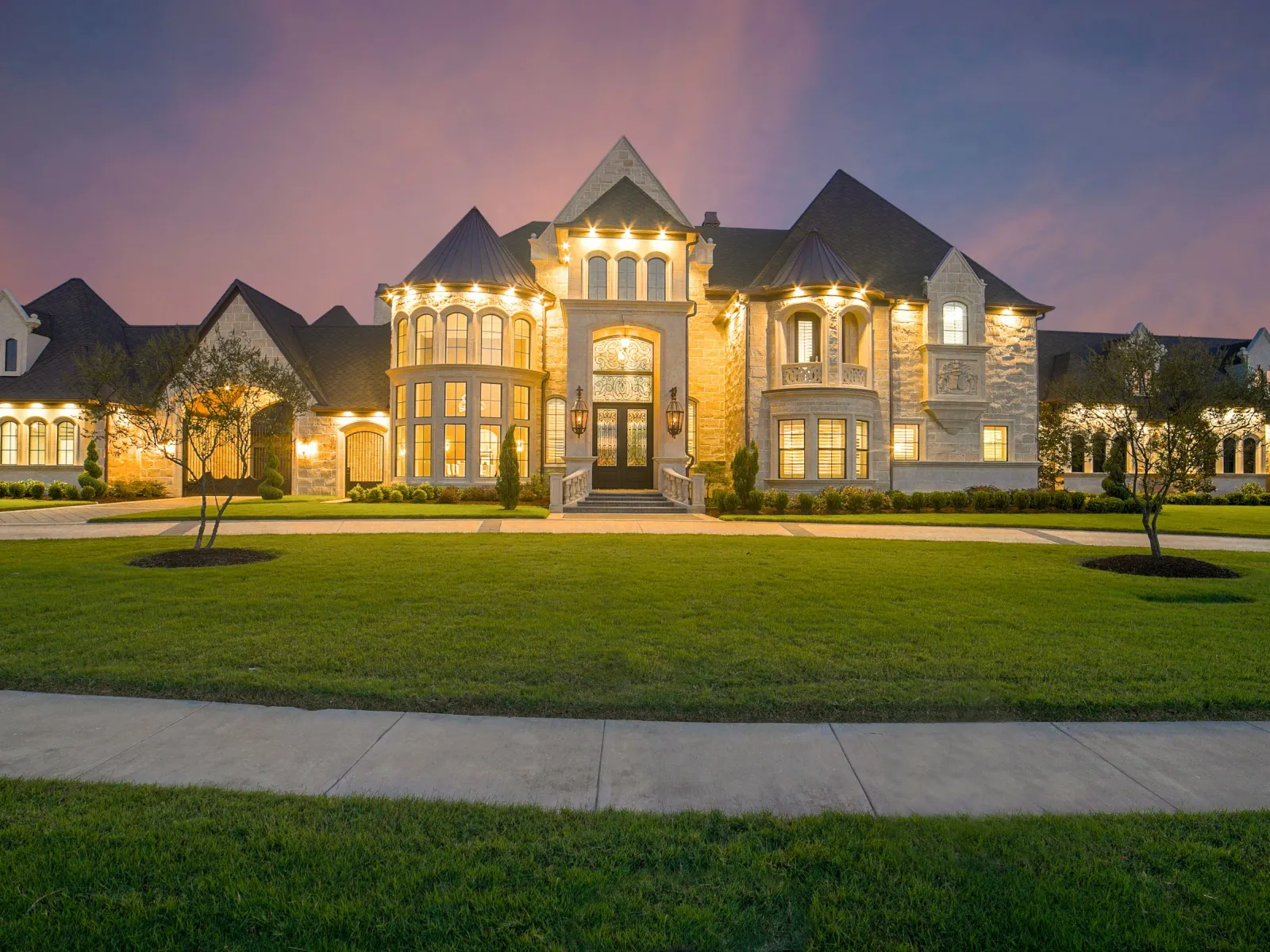 Luxurious illuminated mansion with manicured lawn and twilight sky in the background.