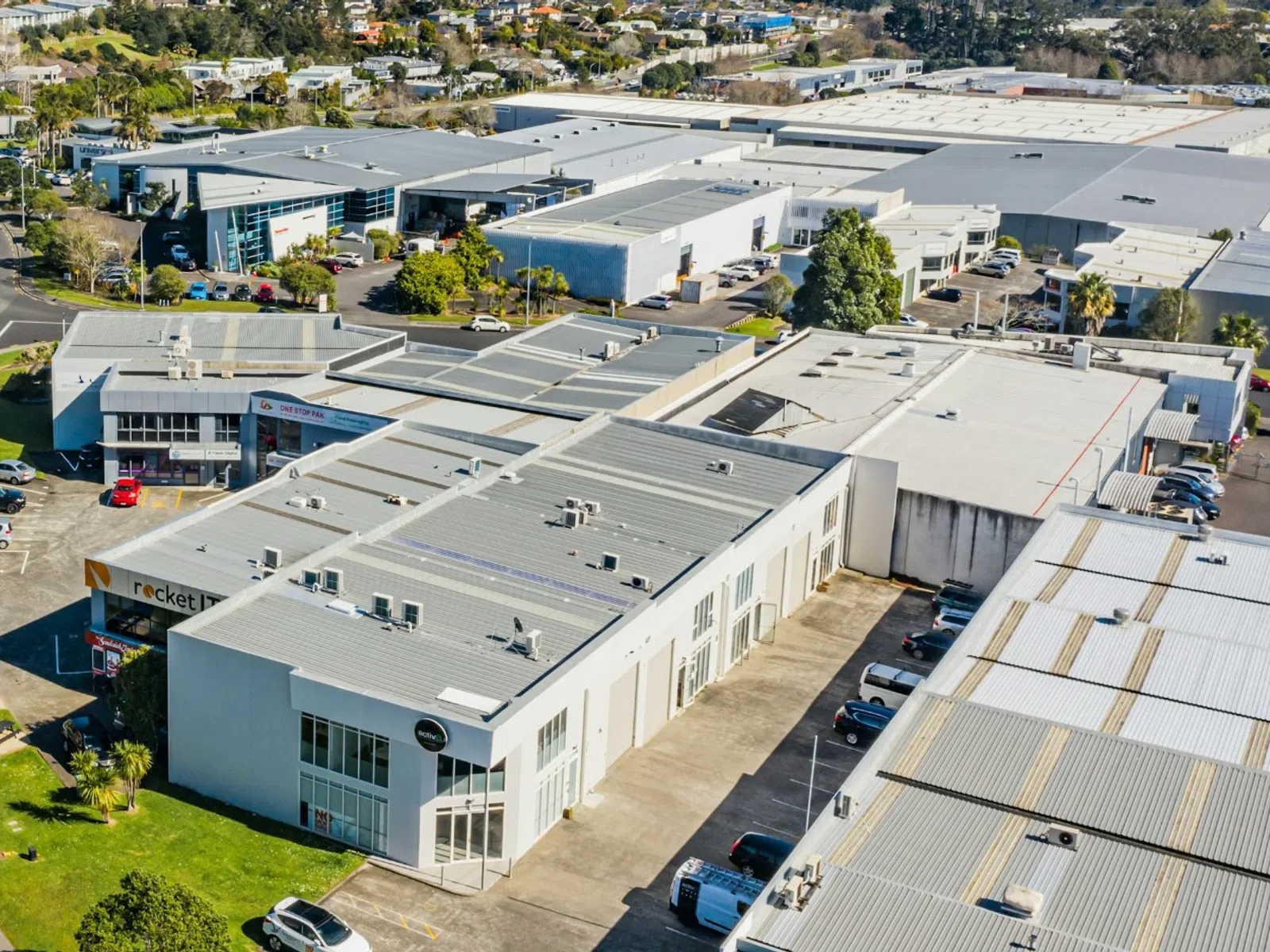 Aerial view of an industrial park with warehouses, offices, and a curved street with cars and greenery.