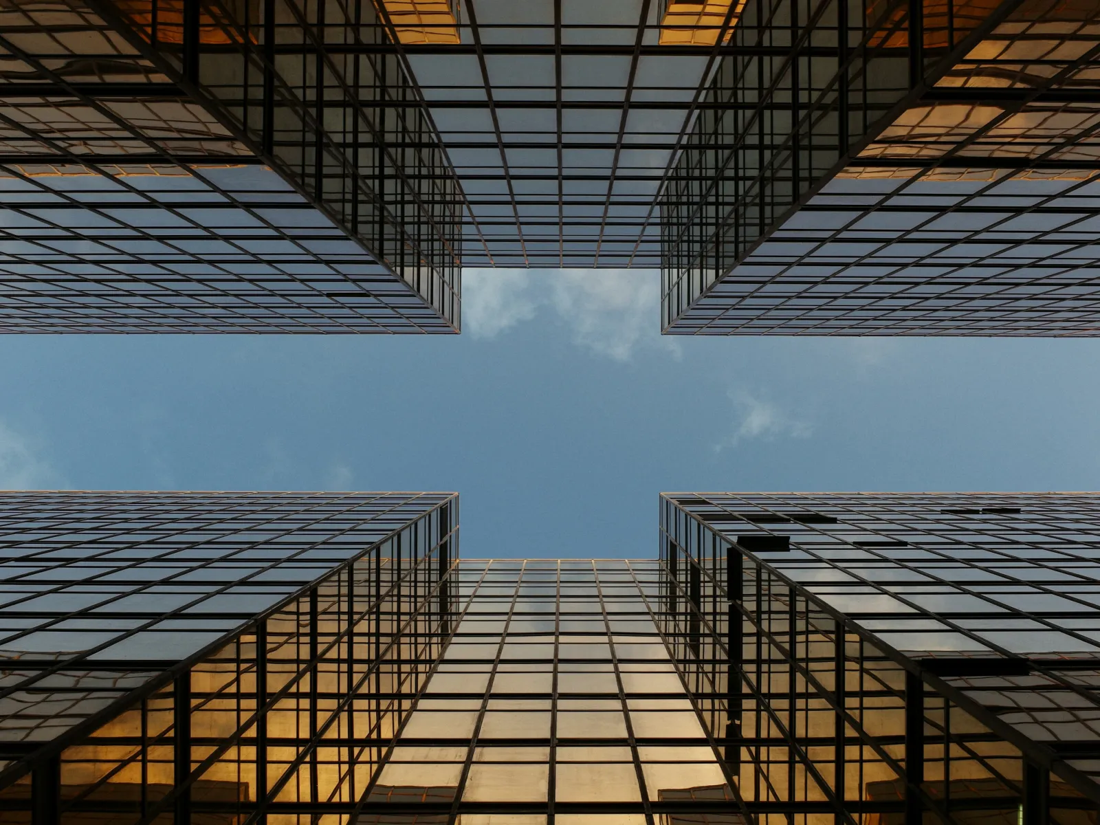 View looking up at modern glass skyscrapers with a blue sky in the center.