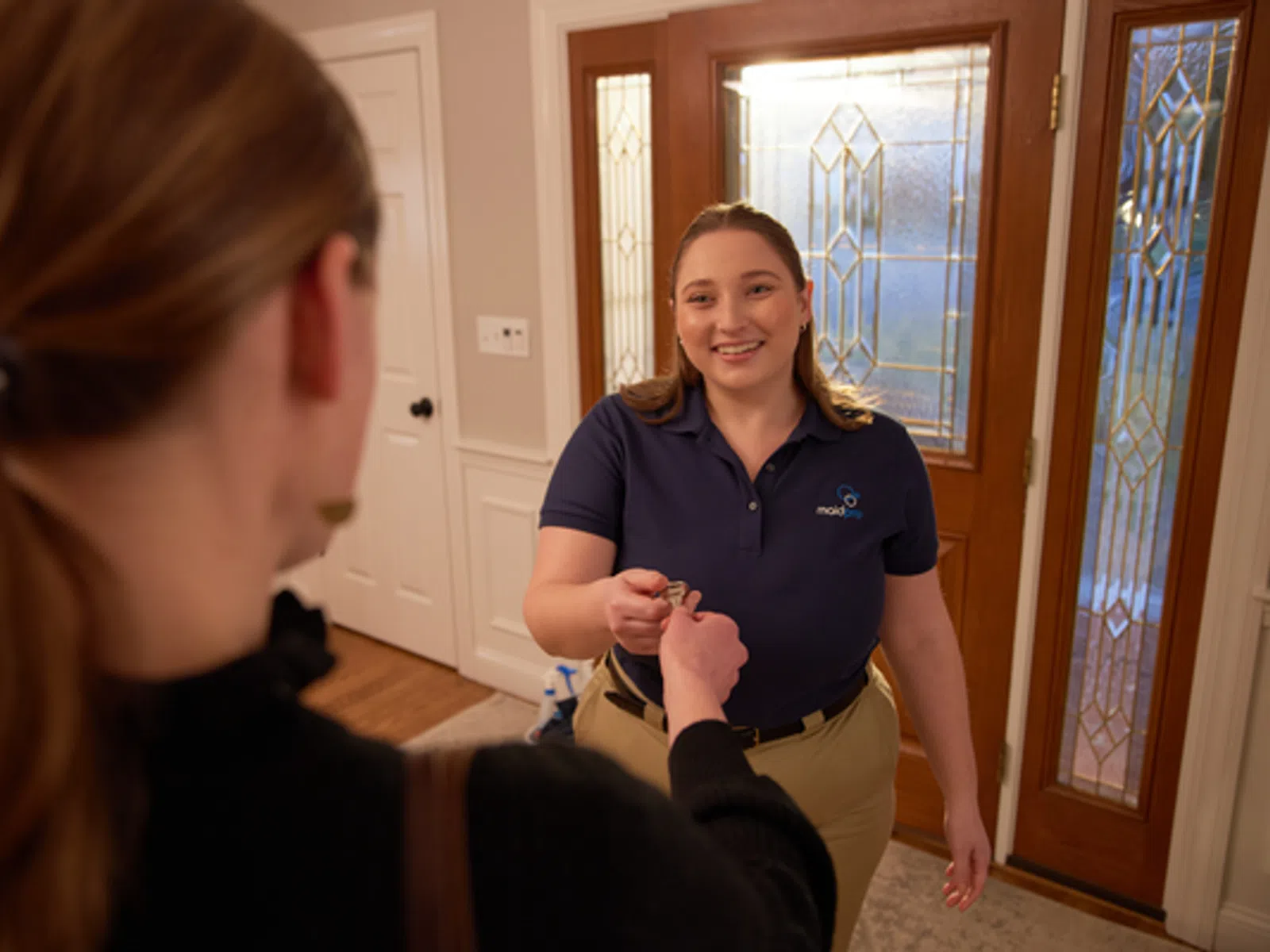 Home service worker handing keys to a smiling customer inside a warmly lit entryway with decorative glass doors.