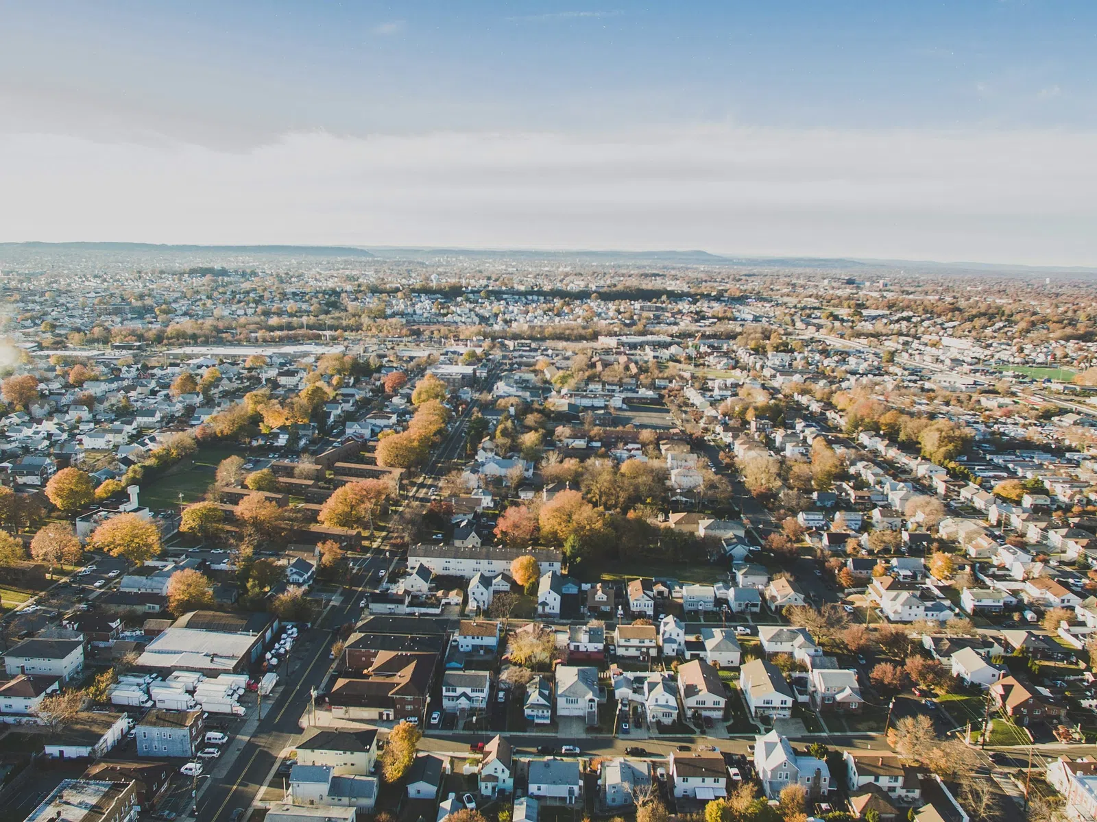 Aerial view of a suburban neighborhood with houses, streets, and autumn trees under a clear sky.