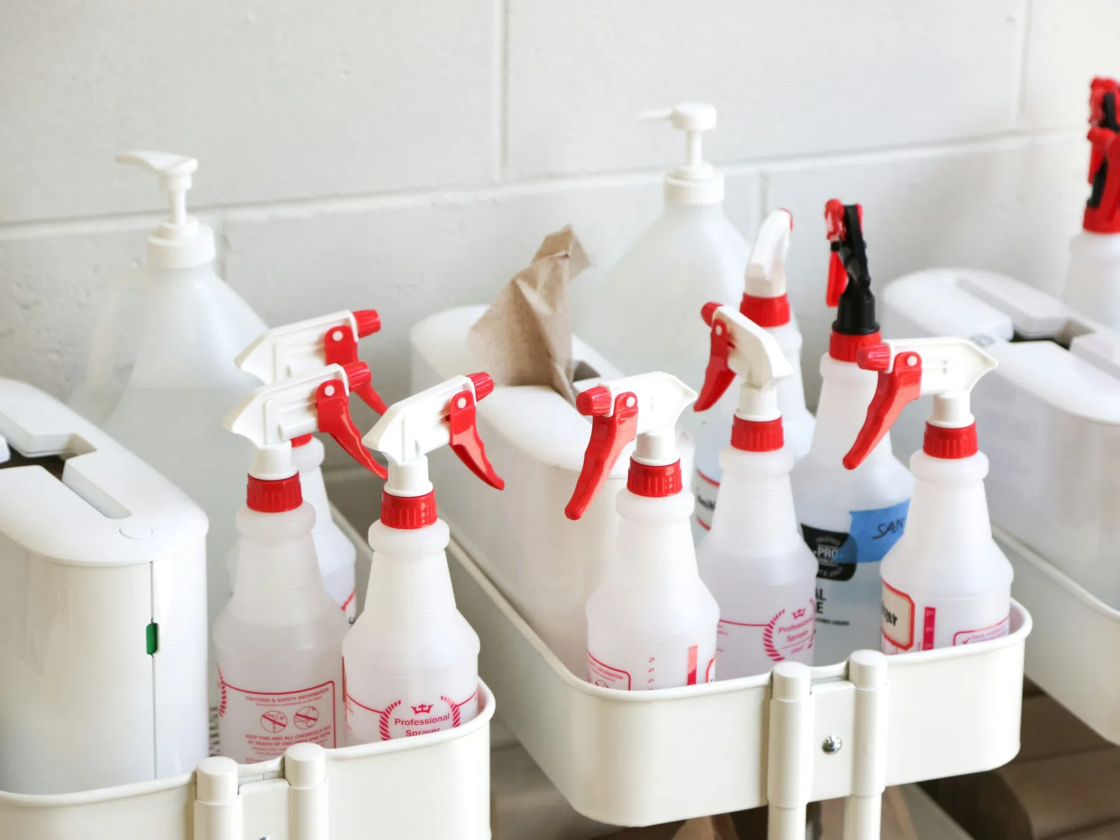 Assorted cleaning spray bottles organized in a storage cart, showcasing diverse cleaning supplies and tools.