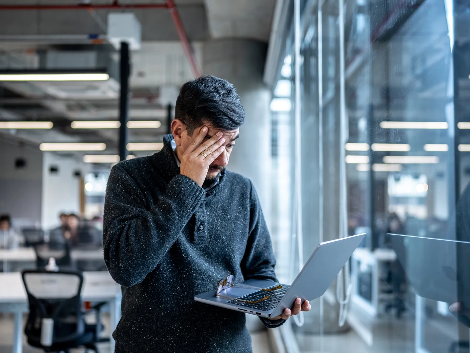 a man holding a tablet and looking at a laptop