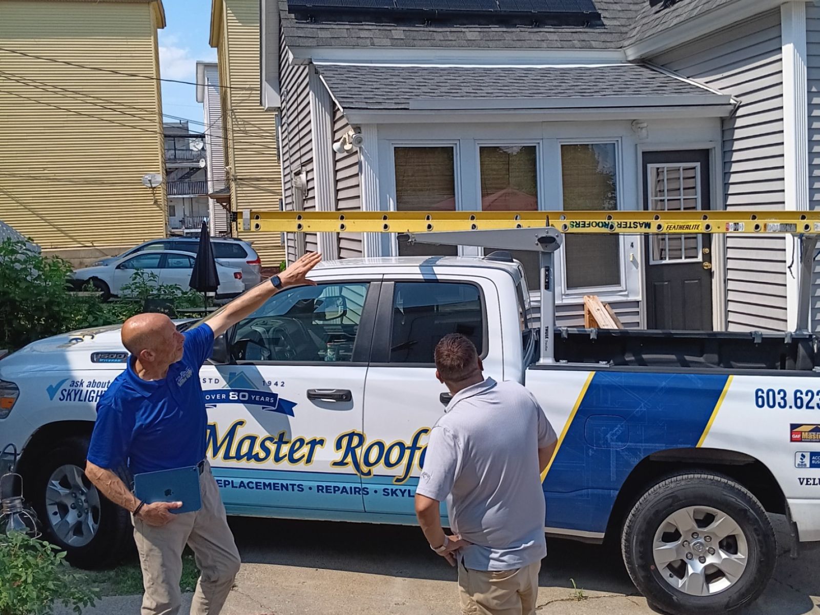 Two contractors discussing roofing work next to a branded truck under a clear blue sky.
