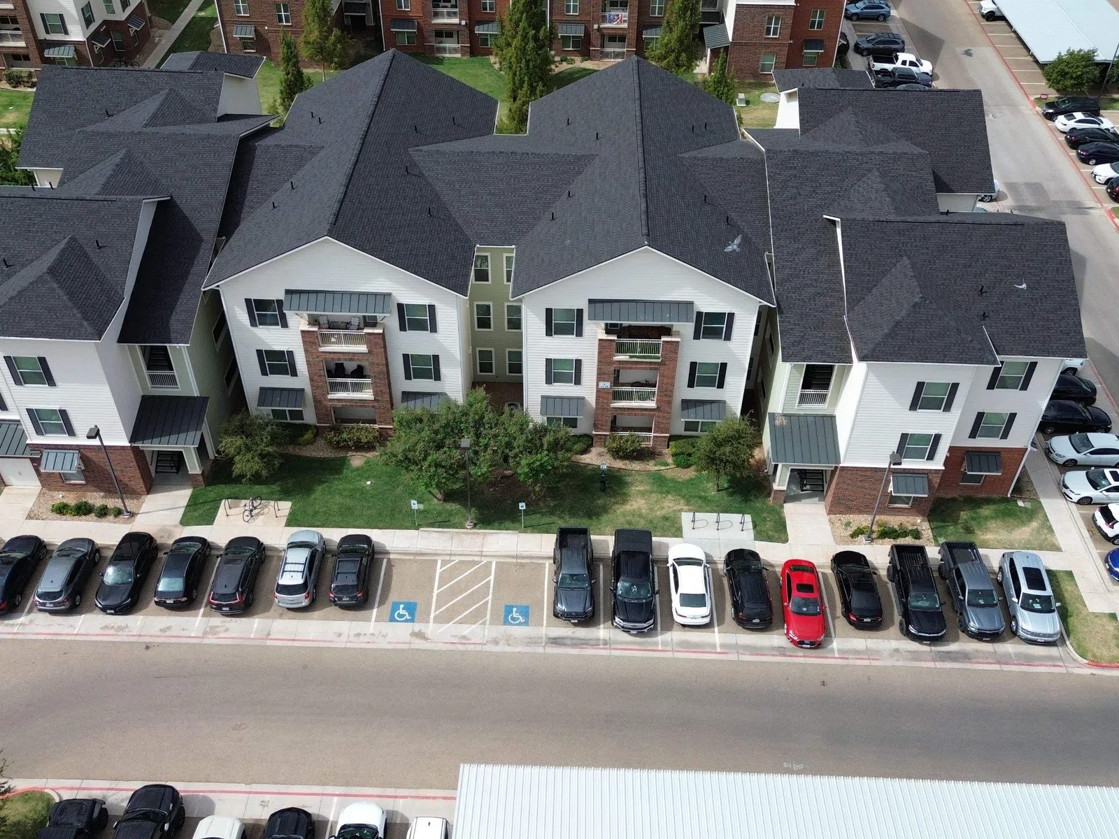 Aerial view of modern apartment buildings with parked cars and green landscaping around.