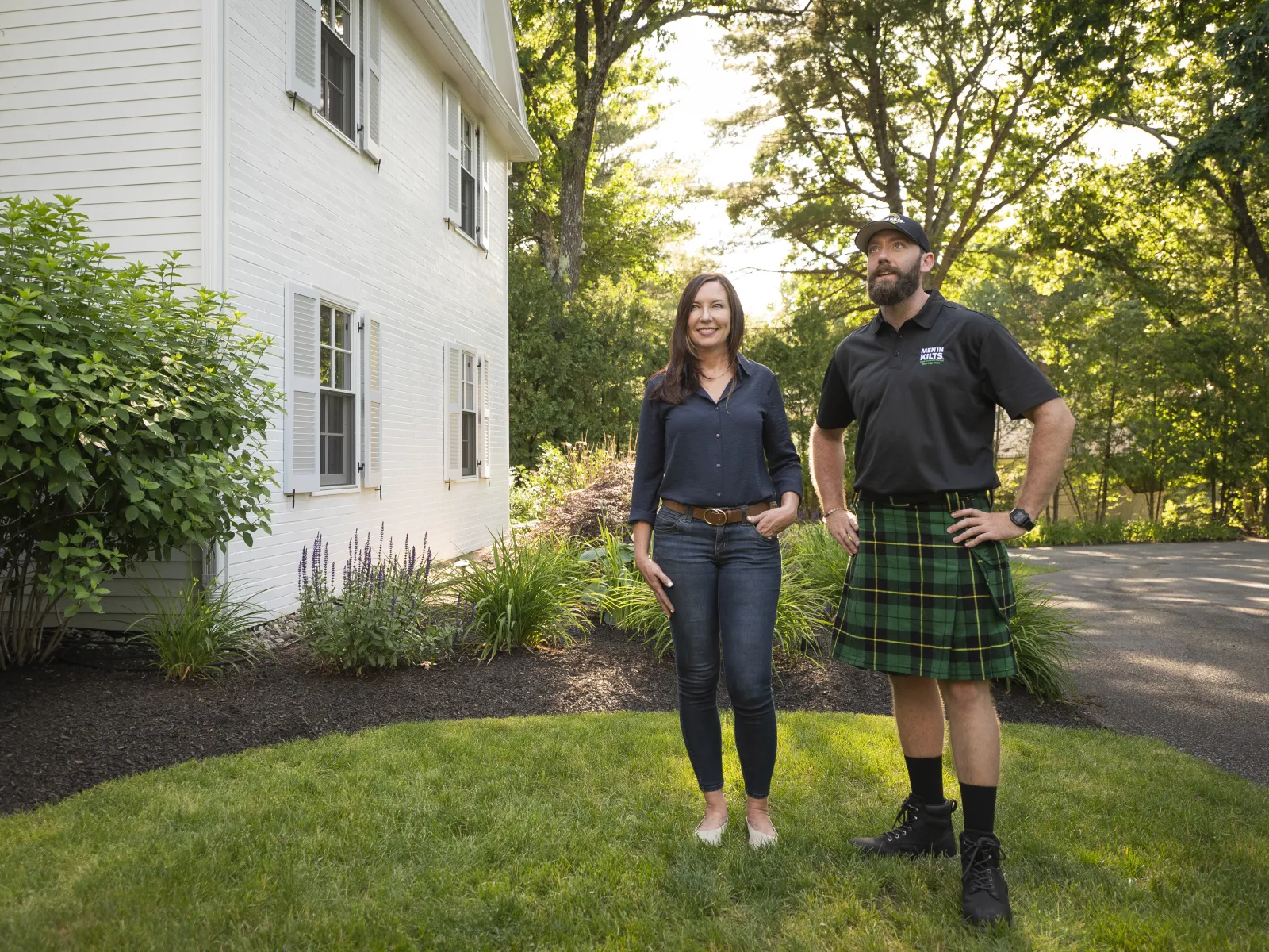 a man and woman standing in a yard with a house and trees