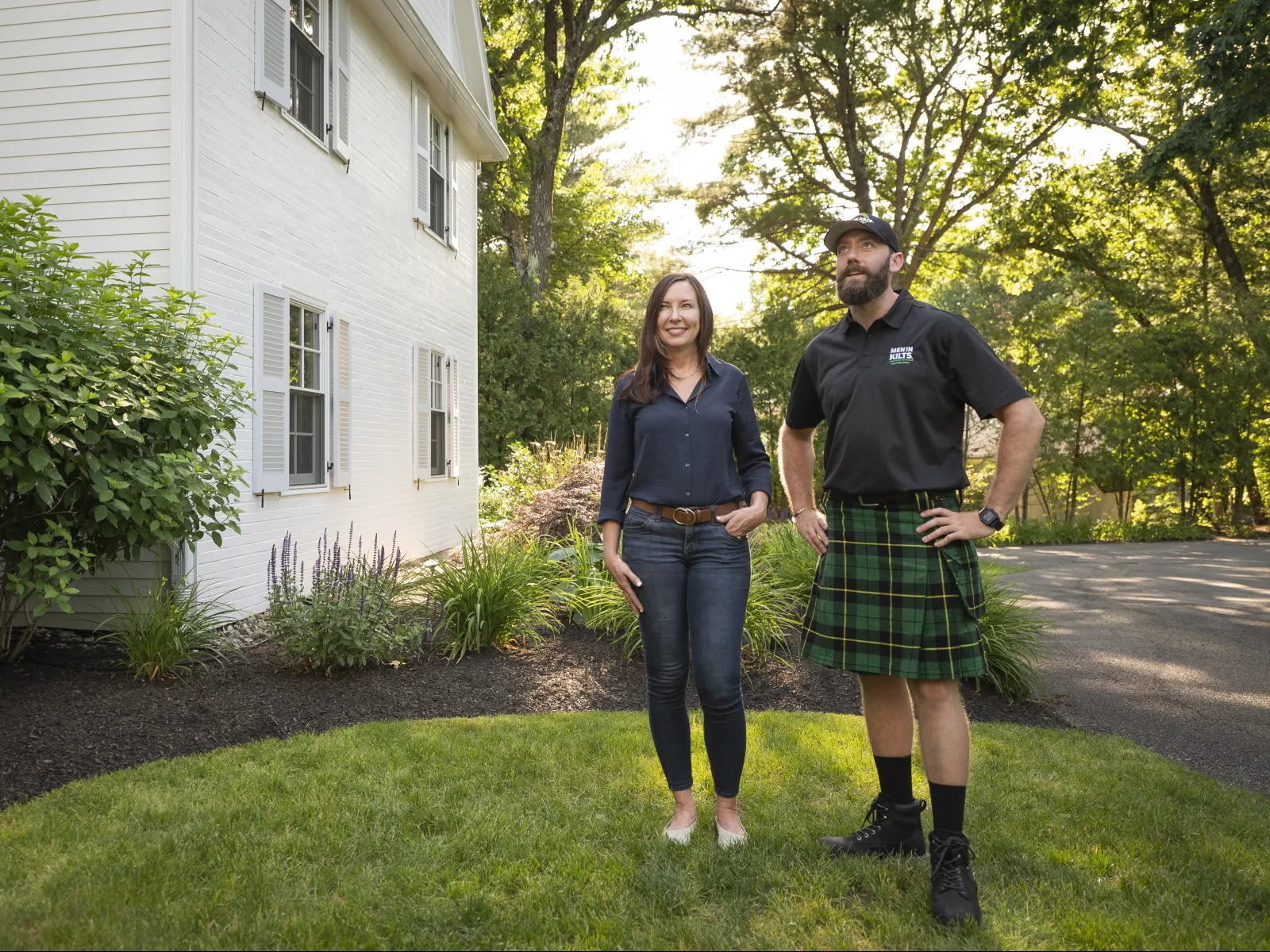 a man and woman standing in a yard with a house and trees