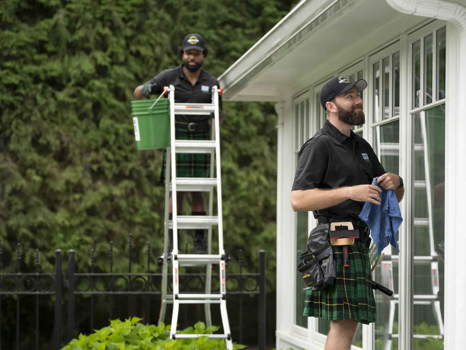 a couple of men standing on a ladder with a green bin on it