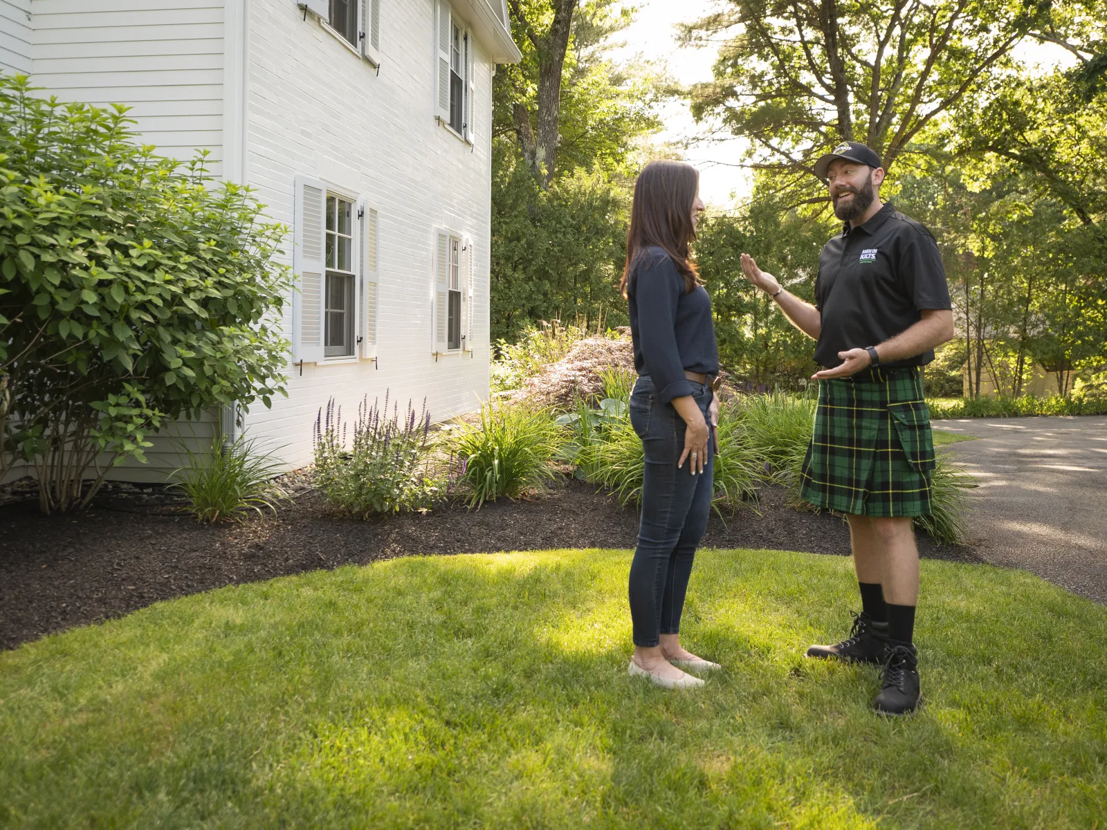 a man and a woman standing in a yard with a house and trees