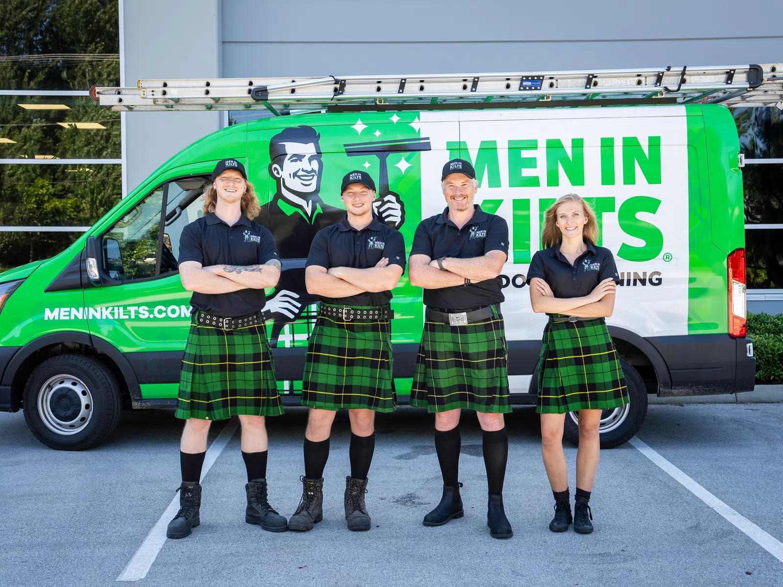 Four men and one woman wearing green plaid kilts and black shirts standing in front of a green Men In Kilts van.