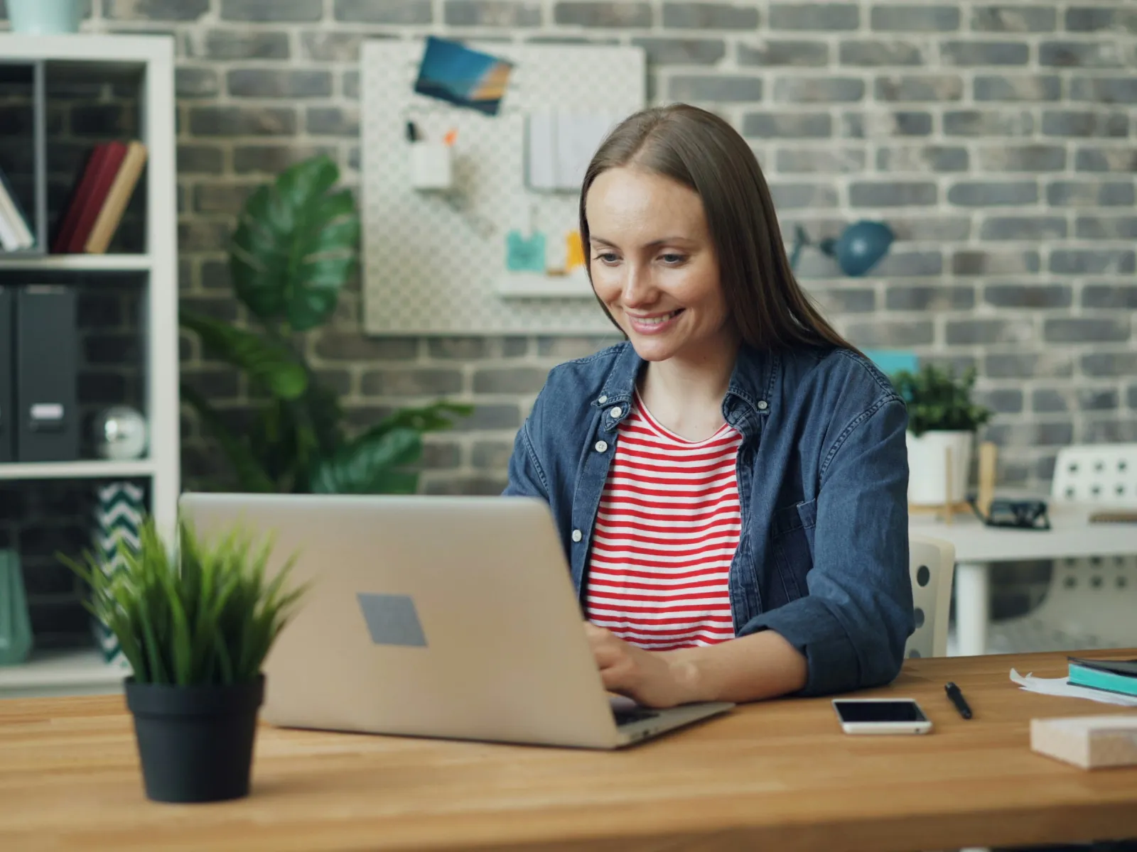 Smiling woman working on a laptop at a modern home office with plants and decor.