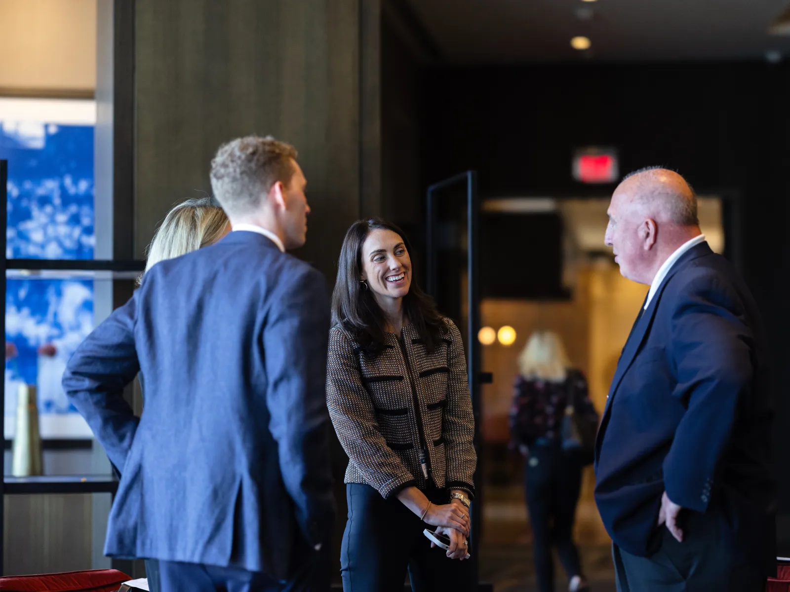 Group of professionals in business attire conversing in a modern office lobby with warm lighting