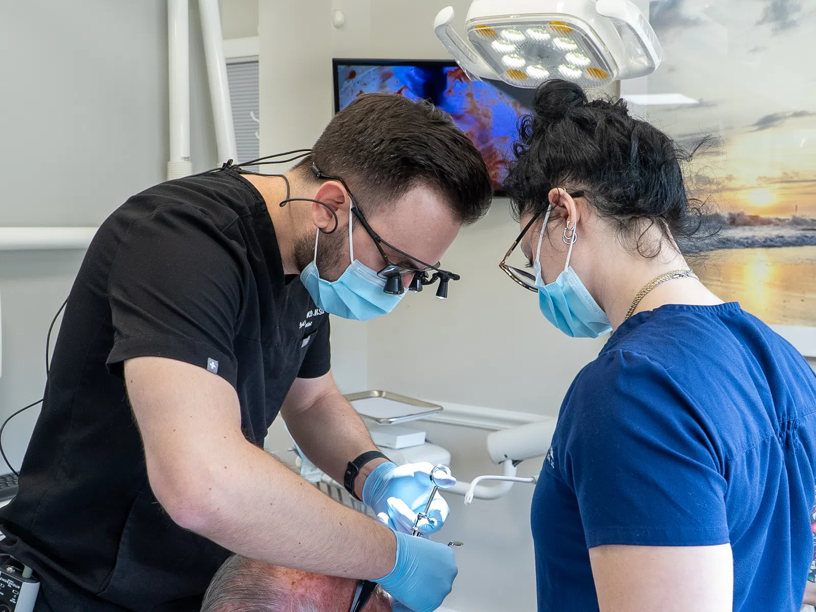 Dentist and dental assistant wearing masks performing a dental procedure on a patient in a clinic.
