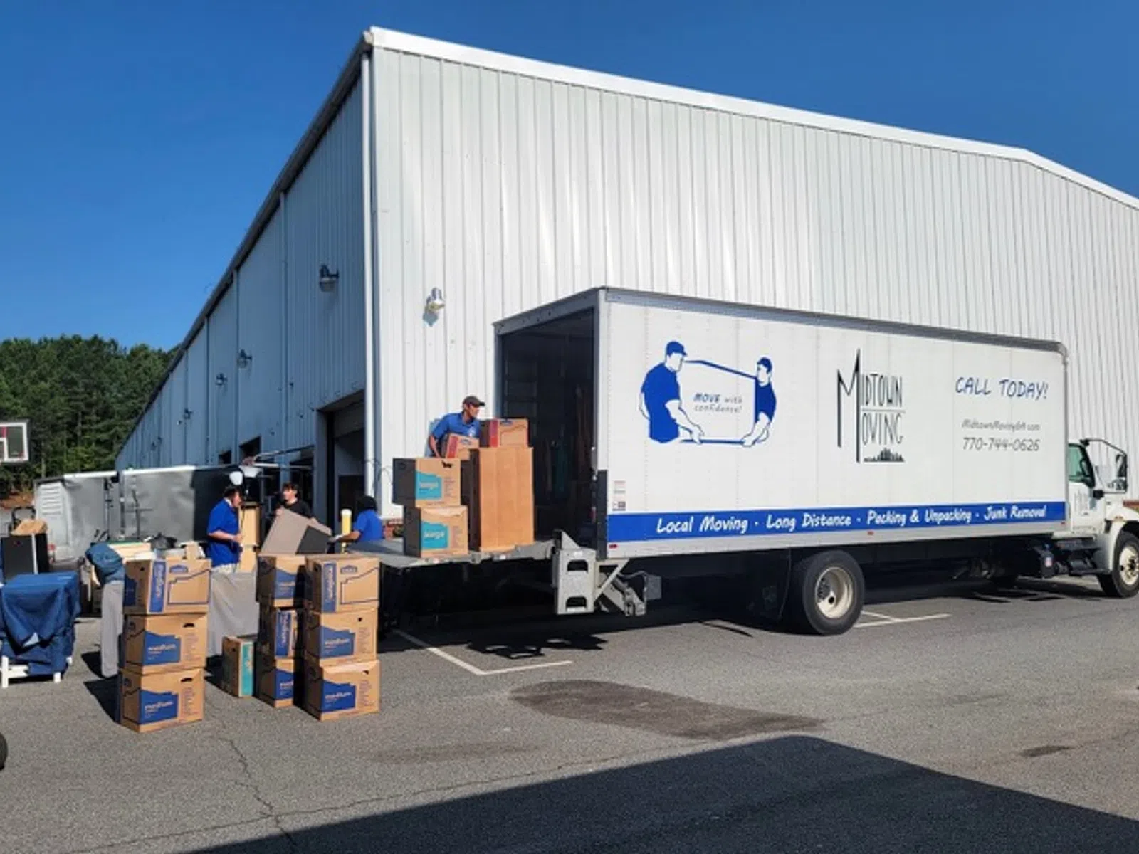 Midtown Moving truck being loaded with boxes by movers outside a warehouse on a sunny day.