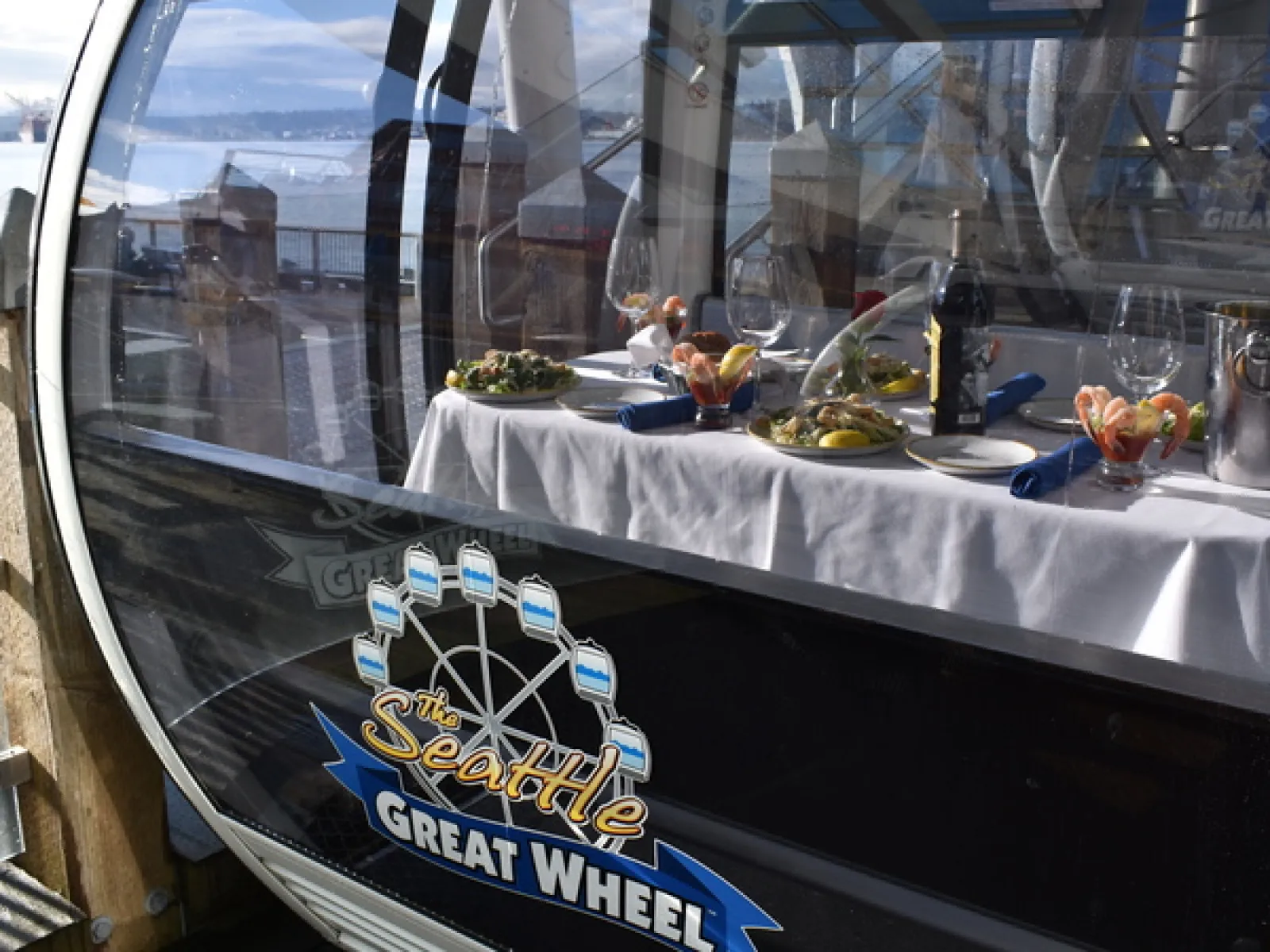 Dining setup inside a Seattle Great Wheel gondola with table, seafood, wine, and waterfront view.