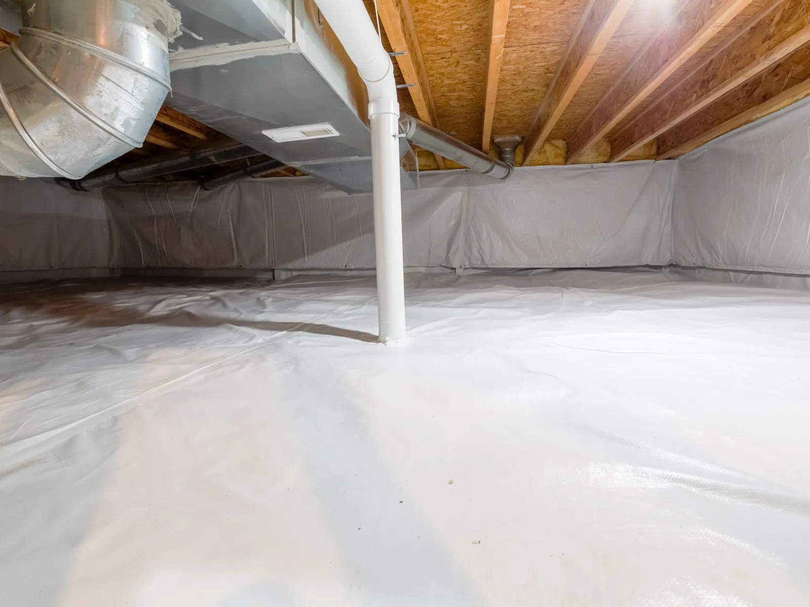 Clean crawl space with white vapor barrier covering floor and walls and exposed wooden beams on ceiling.