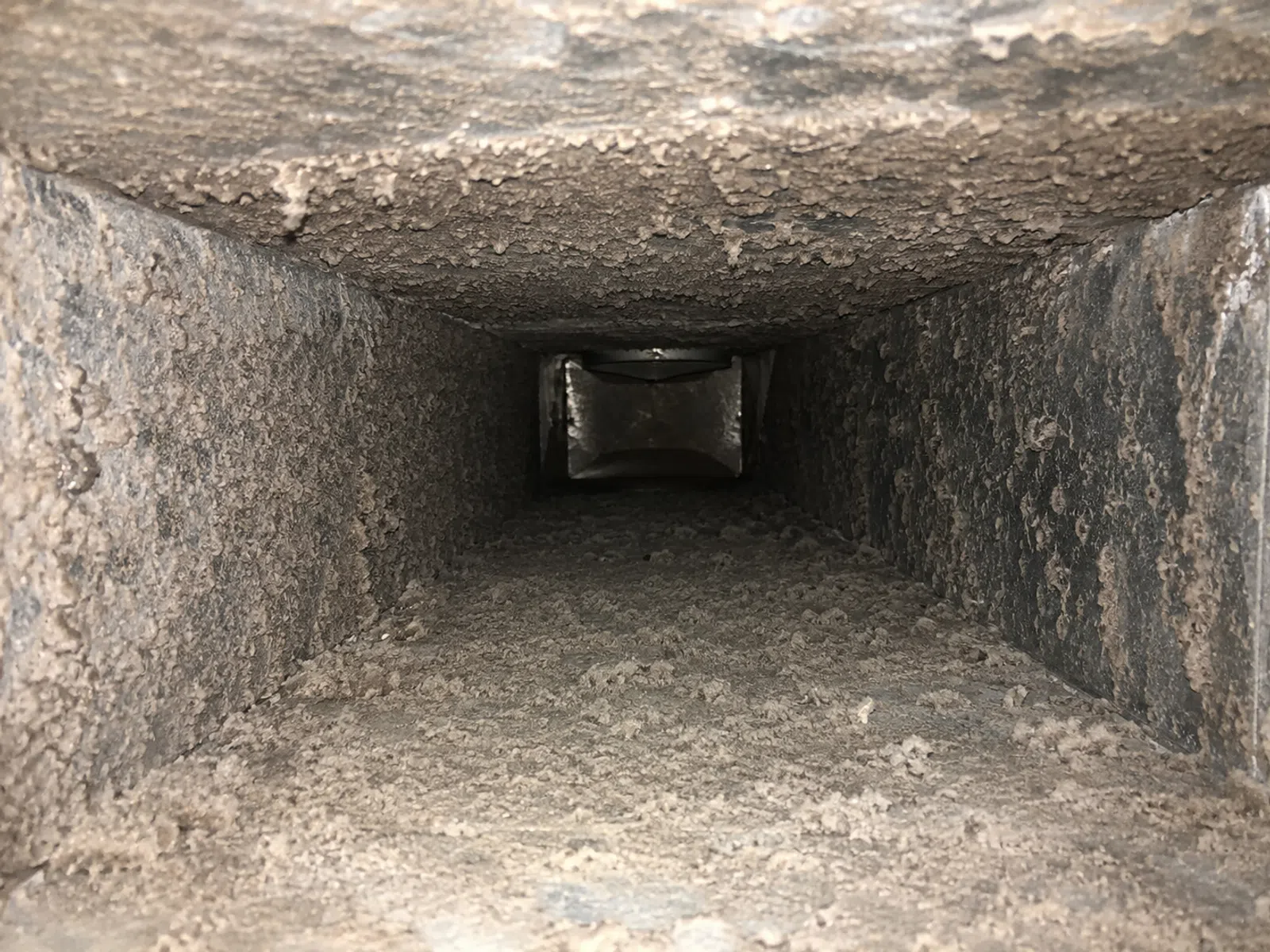 Interior view of a heavily dust-covered rectangular air duct or ventilation shaft.