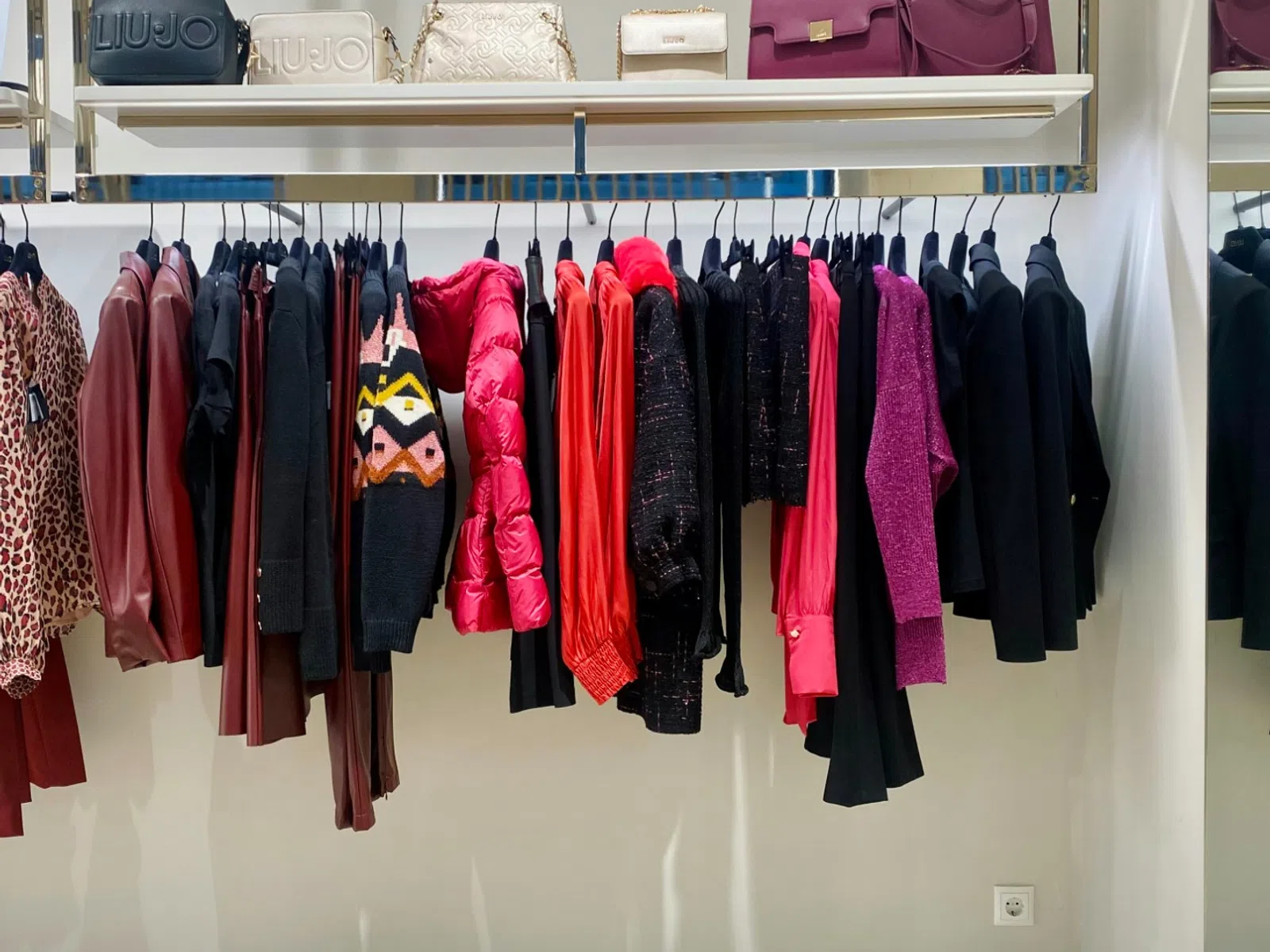 Colorful women's clothing and handbags neatly displayed on rack and shelf in a boutique store
