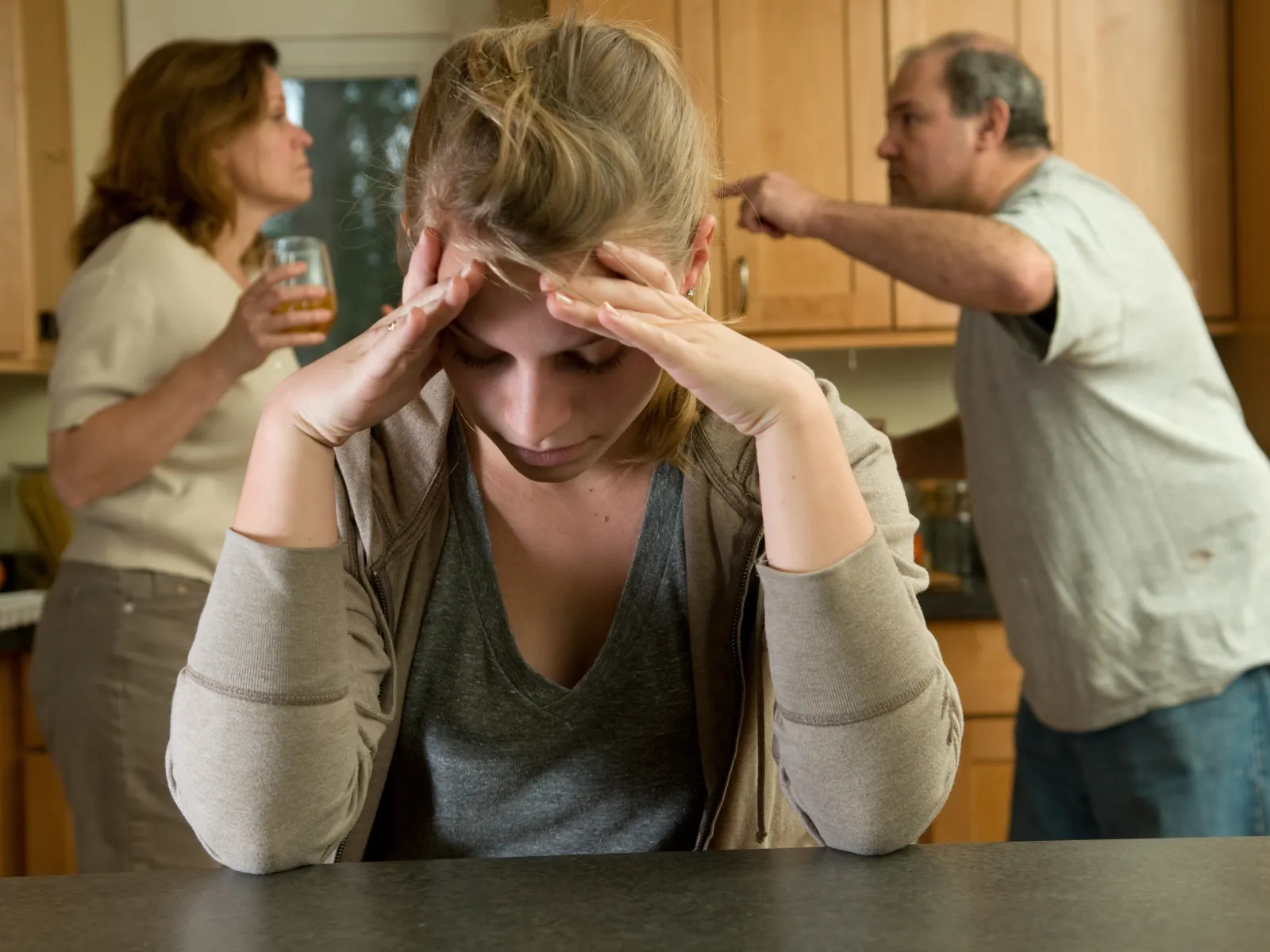 Consequences of Parental Alienation: older child looks down at table while parents are fighting.