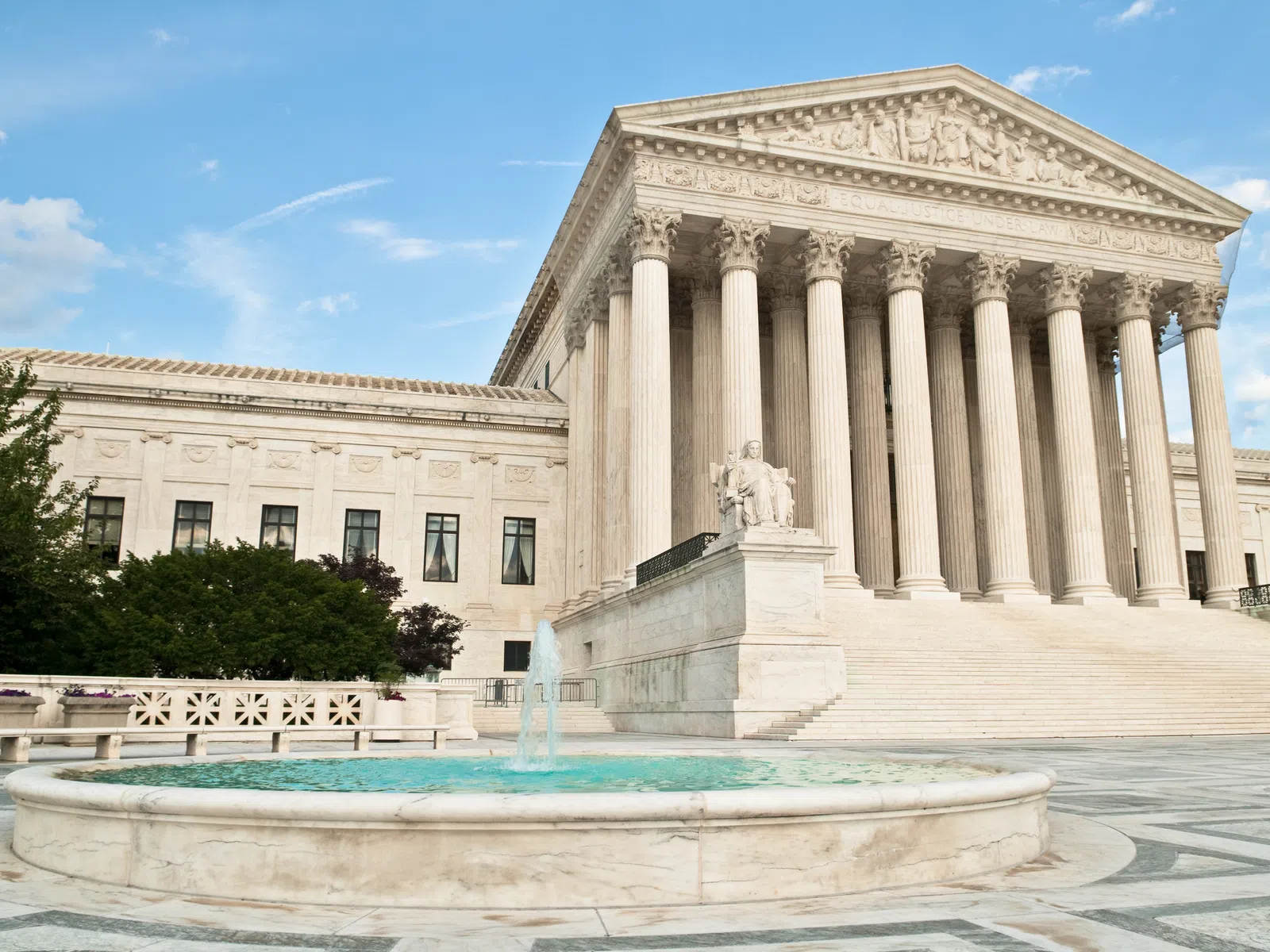 The United States Supreme Court building with tall columns, steps, a fountain, and blue sky in Washington D.C.