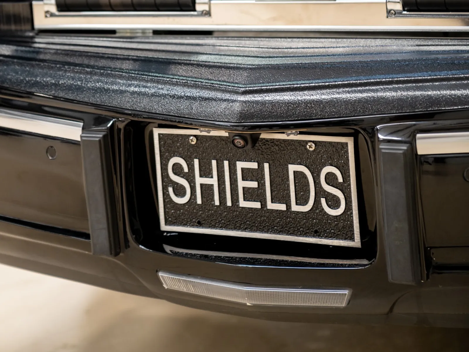 Close-up of a black shield casket with handles and a 'SHIELDS' license plate on the back of a vehicle.